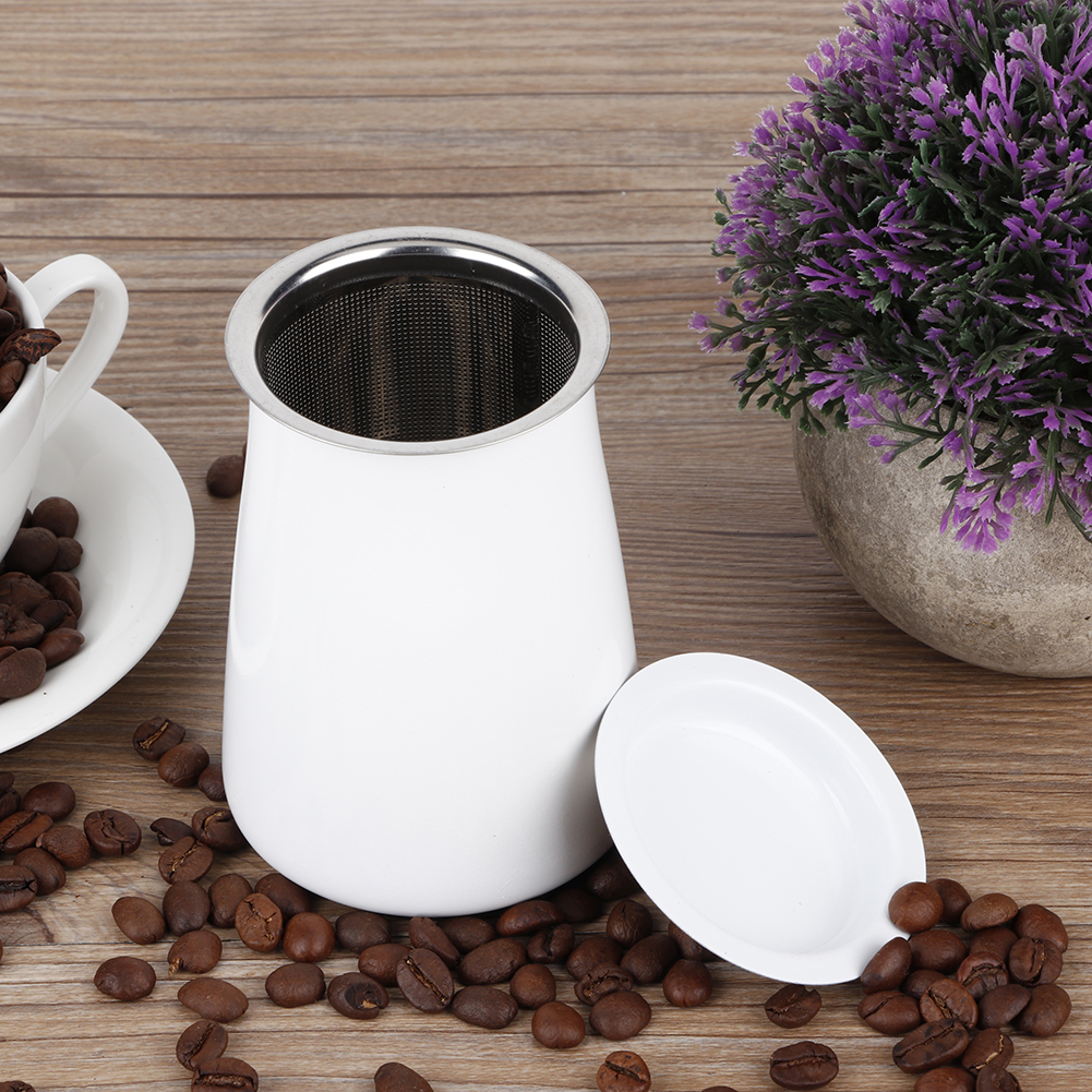 Ein weißer Kaffeefilter mit Deckel, Kaffeebohnen, eine Tasse und eine lila Pflanze in einem Topf auf Holz.