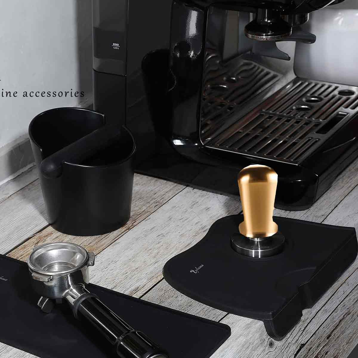 Kaffeemaschinen-Setup mit Zubehör: Tamper, Siebträger und Knock-Box, alles auf einer Holzoberfläche.