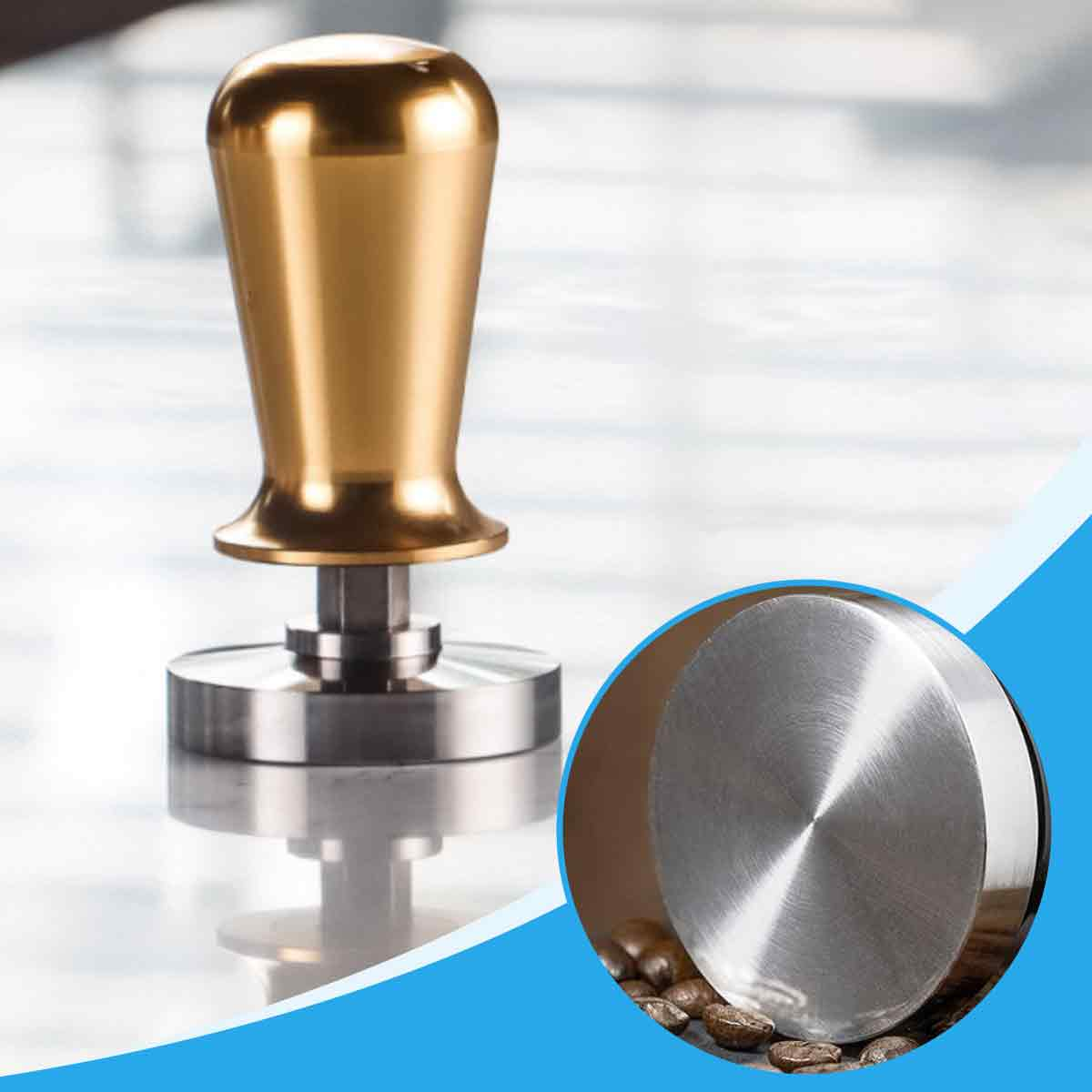 Ein goldener Kaffee-Tamper steht auf einer reflektierenden Oberfläche. Ein kreisförmiges Detail zeigt die Basis mit Kaffeebohnen.