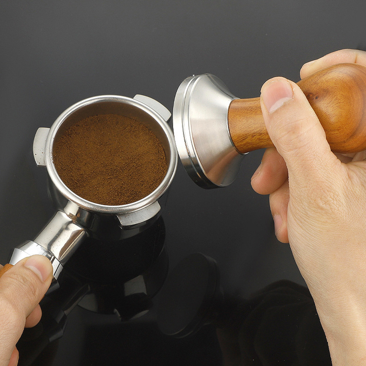 Eine Person hält einen Tamper und einen Siebträger mit Kaffeepulver. Der Tamper hat einen Holzgriff und eine Metallbasis.