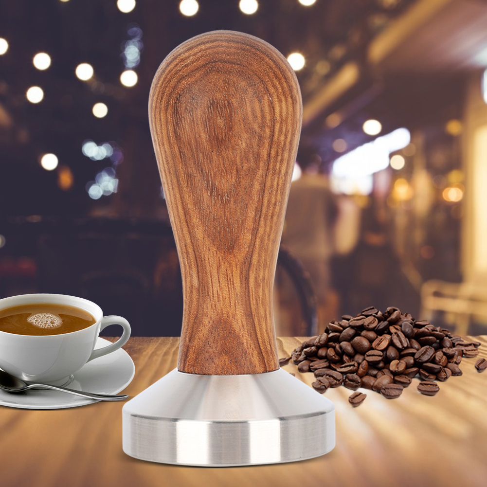 Ein Kaffeestempel mit Holzgriff, Kaffeetasse mit Kaffee und Kaffeebohnen auf einem Holztisch. Verschwommener Hintergrund.