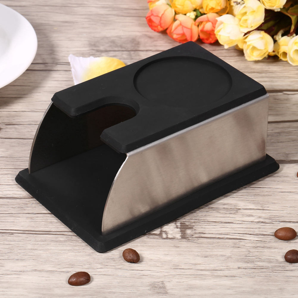 Ein schwarzer und silberner Kaffeetampersockel auf einem Holztisch. Kaffeebohnen sind verstreut. Blumen sind im Hintergrund.