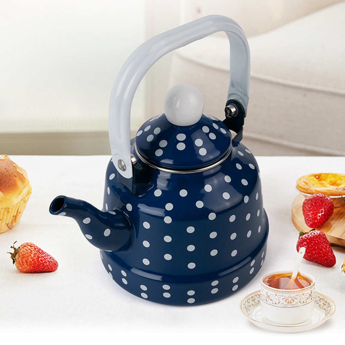 Eine blaue Kanne mit Polka-Dots, Erdbeeren, Gebäck und eine Teetasse auf einer weißen Oberfläche. Die Kanne hat einen weißen Griff.