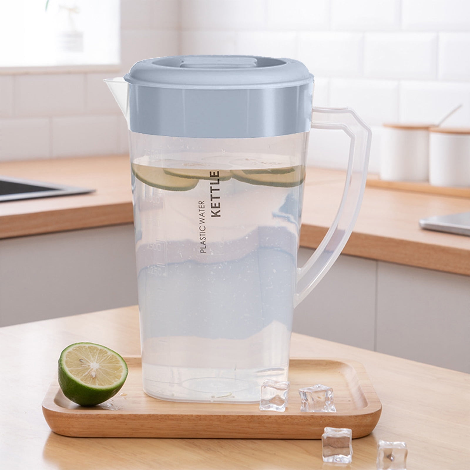 Ein klarer Wasserkrug aus Kunststoff mit Zitronenscheiben und Eiswürfeln auf einem Holztablett. Eine Limette ist links.
