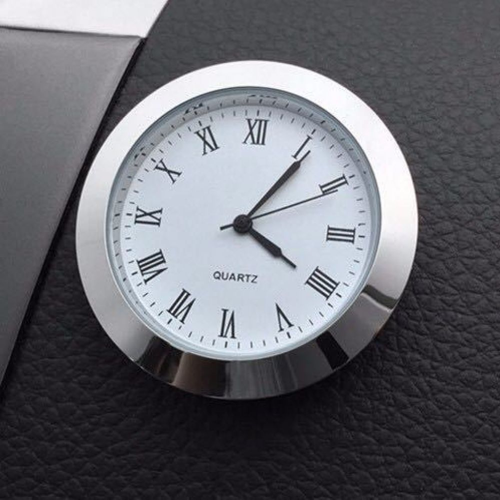 Eine runde Quarzuhr mit römischen Ziffern liegt auf einer schwarzen Oberfläche. Die Uhr hat eine silberne Lünette und schwarze Zeiger.