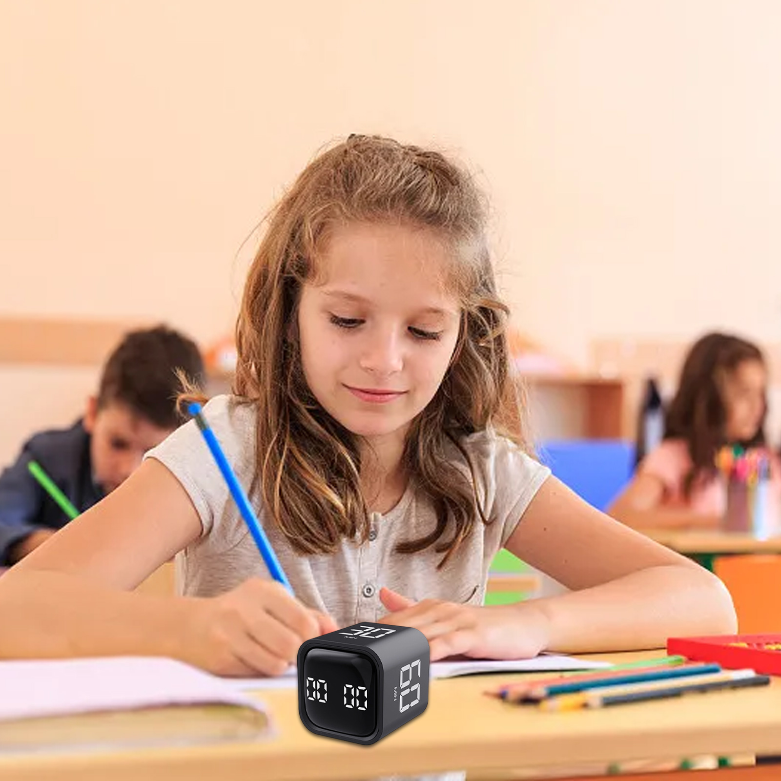 Ein Mädchen schreibt an einem Schreibtisch mit einem Timer. Zwei andere Schüler sind im Hintergrund.
