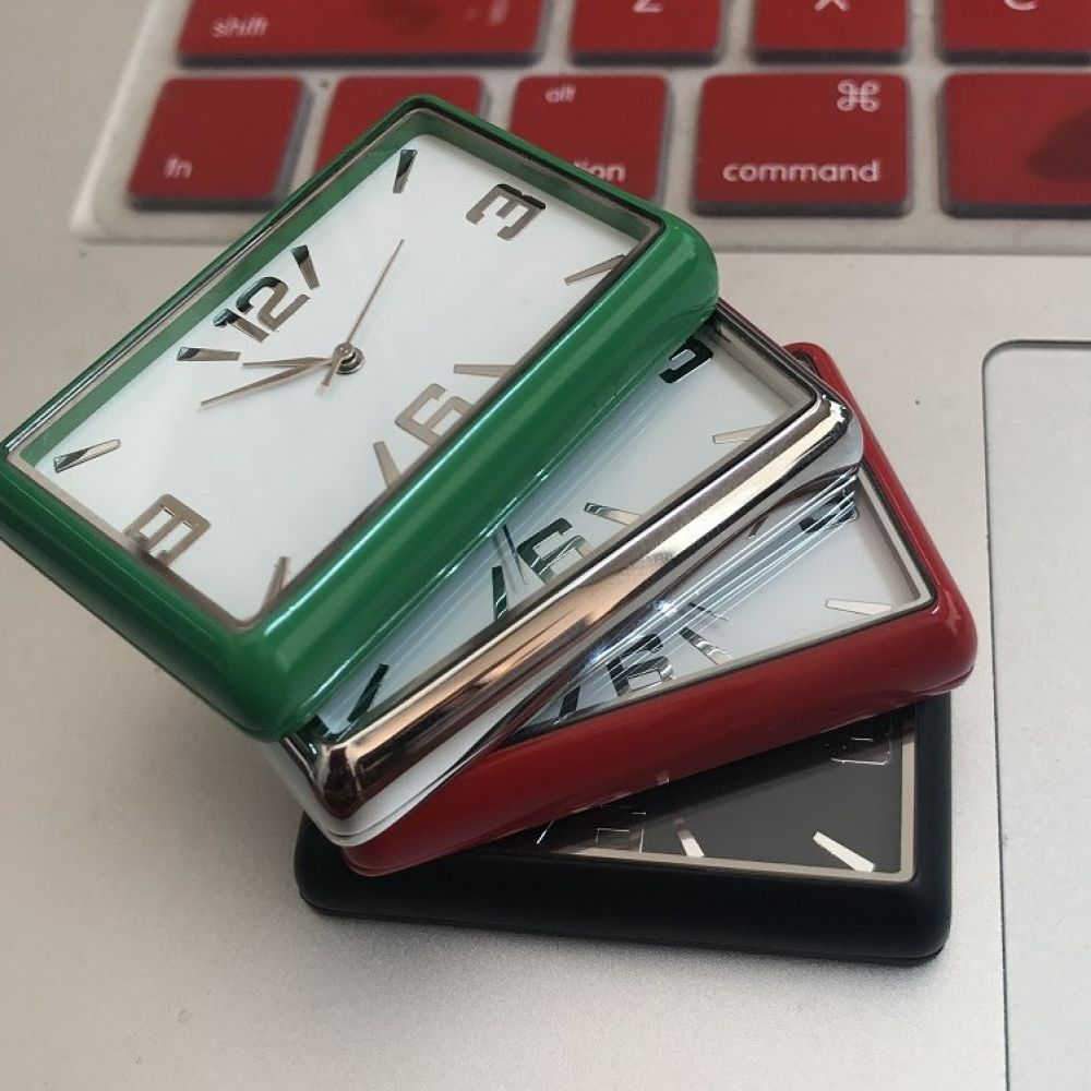 Drei rechteckige Uhren, grün, silber, rot und schwarz, auf einem Laptop gestapelt. Die Tastatur ist im Hintergrund sichtbar.