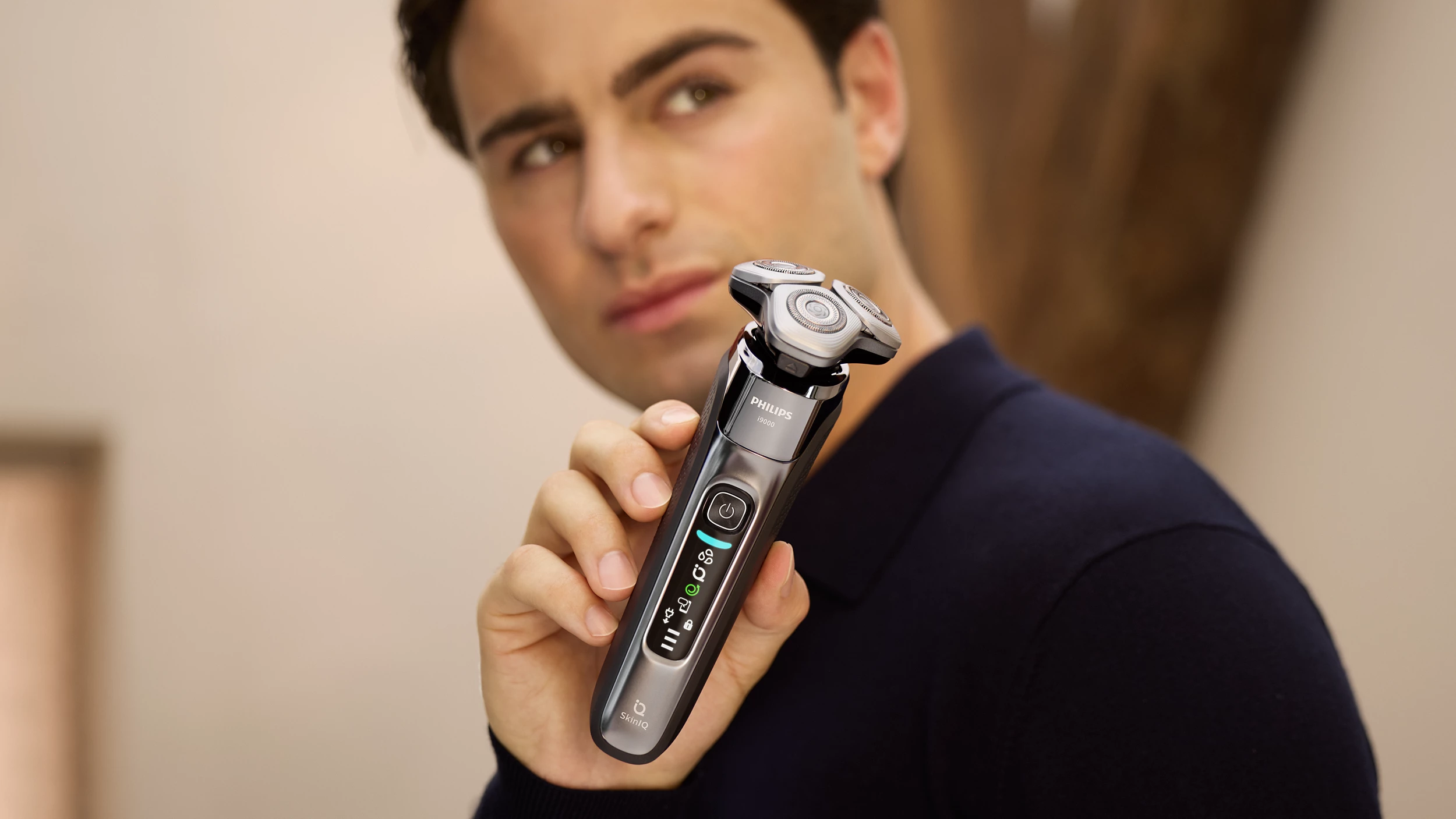 Un uomo tiene un rasoio Philips. Il rasoio è nero e argento. L'uomo indossa una camicia blu navy.