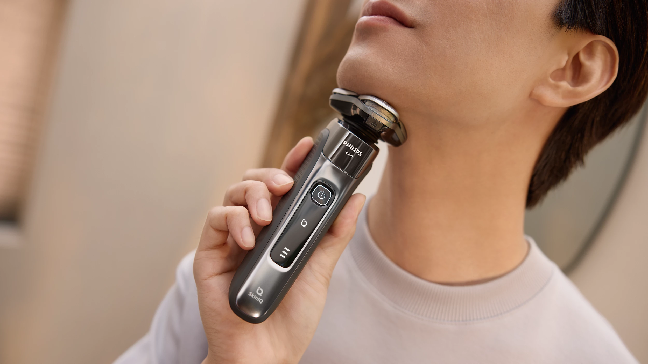 Una persona si rade il collo con un rasoio elettrico Philips. Il rasoio è grigio e nero. La persona indossa una camicia bianca.