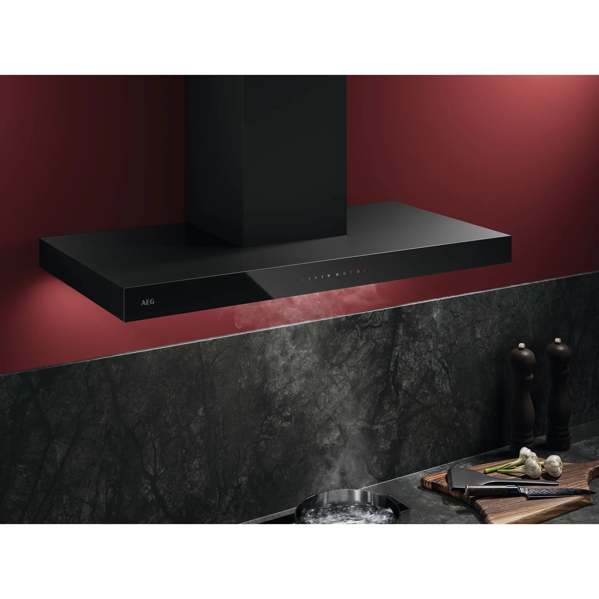 Black range hood above a stove. Garlic, a knife, and pepper grinders are on a wooden cutting board.