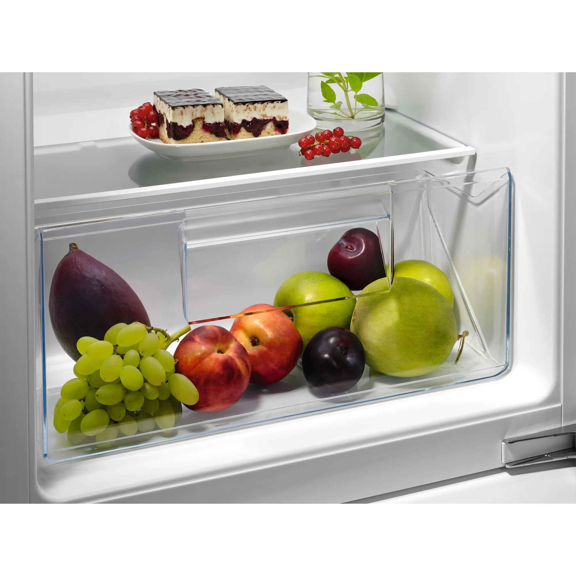 Interno di un frigorifero con frutta, torta e acqua alle erbe. La frutta comprende uva, prugne, pesche e pere.