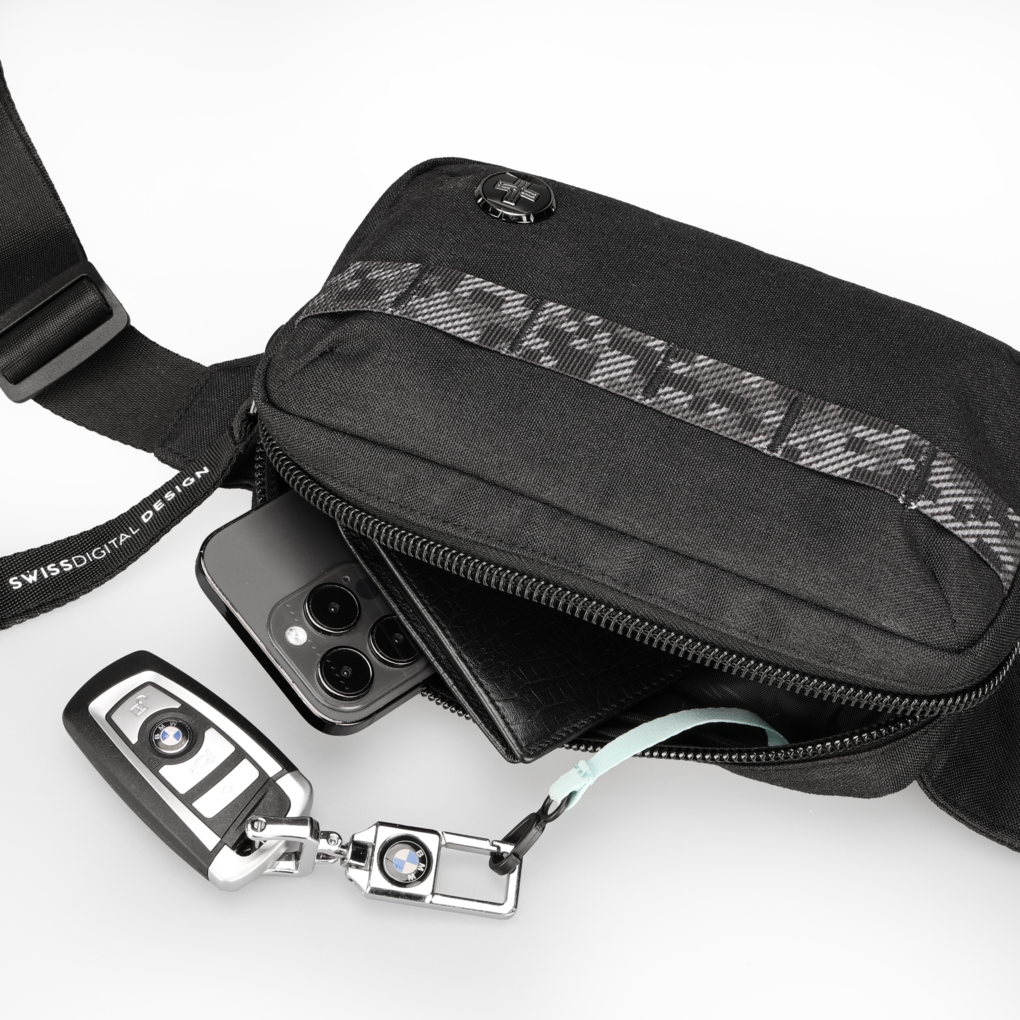 Borsa a tracolla nera con contenuto: telefono, portafoglio, chiave auto. Sfondo bianco. Etichetta Swiss Digital Design.