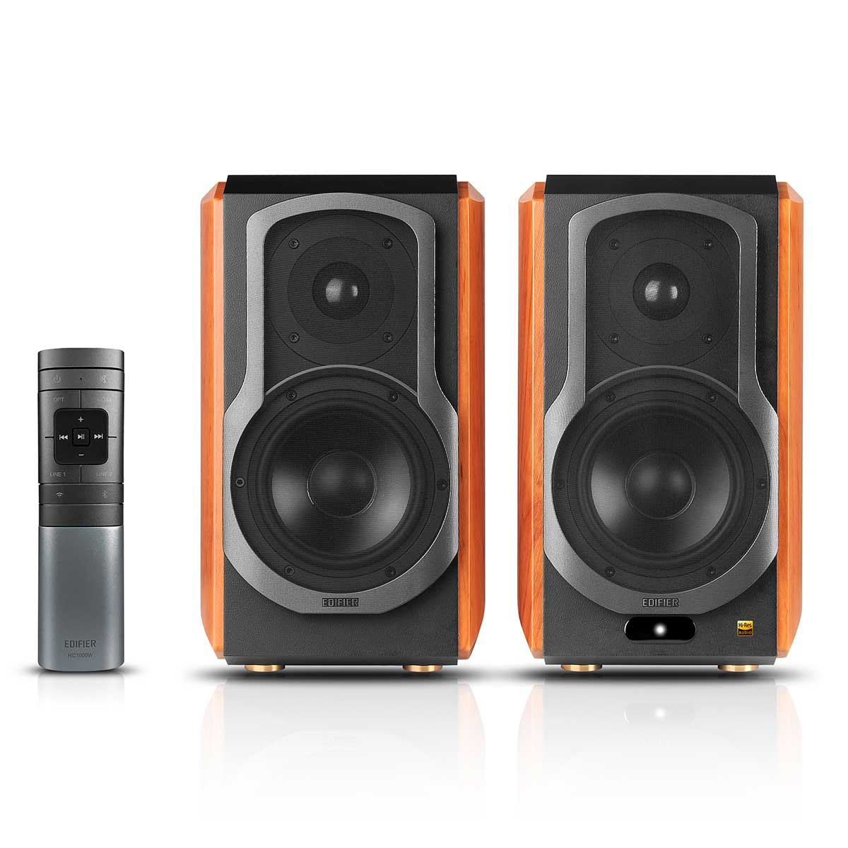 Dwa drewniane głośniki z czarnymi frontami i pilotem na białej powierzchni. Głośniki mają srebrne i czarne akcenty.