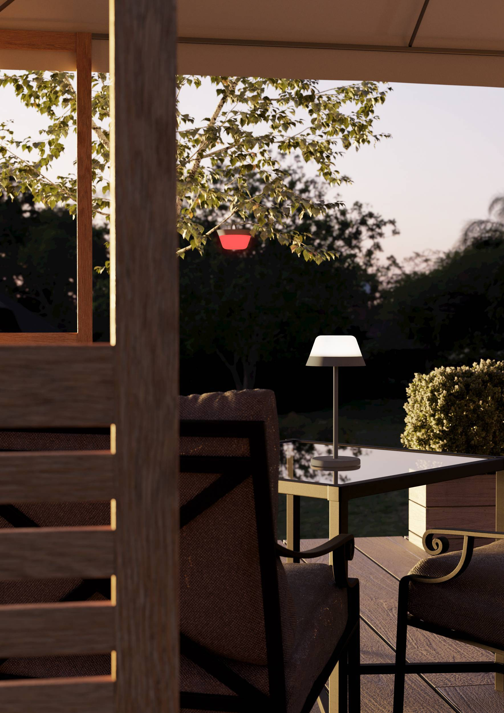 Szene im Freien bei Dämmerung. Tisch mit Lampe und Stühlen auf Holzterrasse. Rotes Licht im Baum.