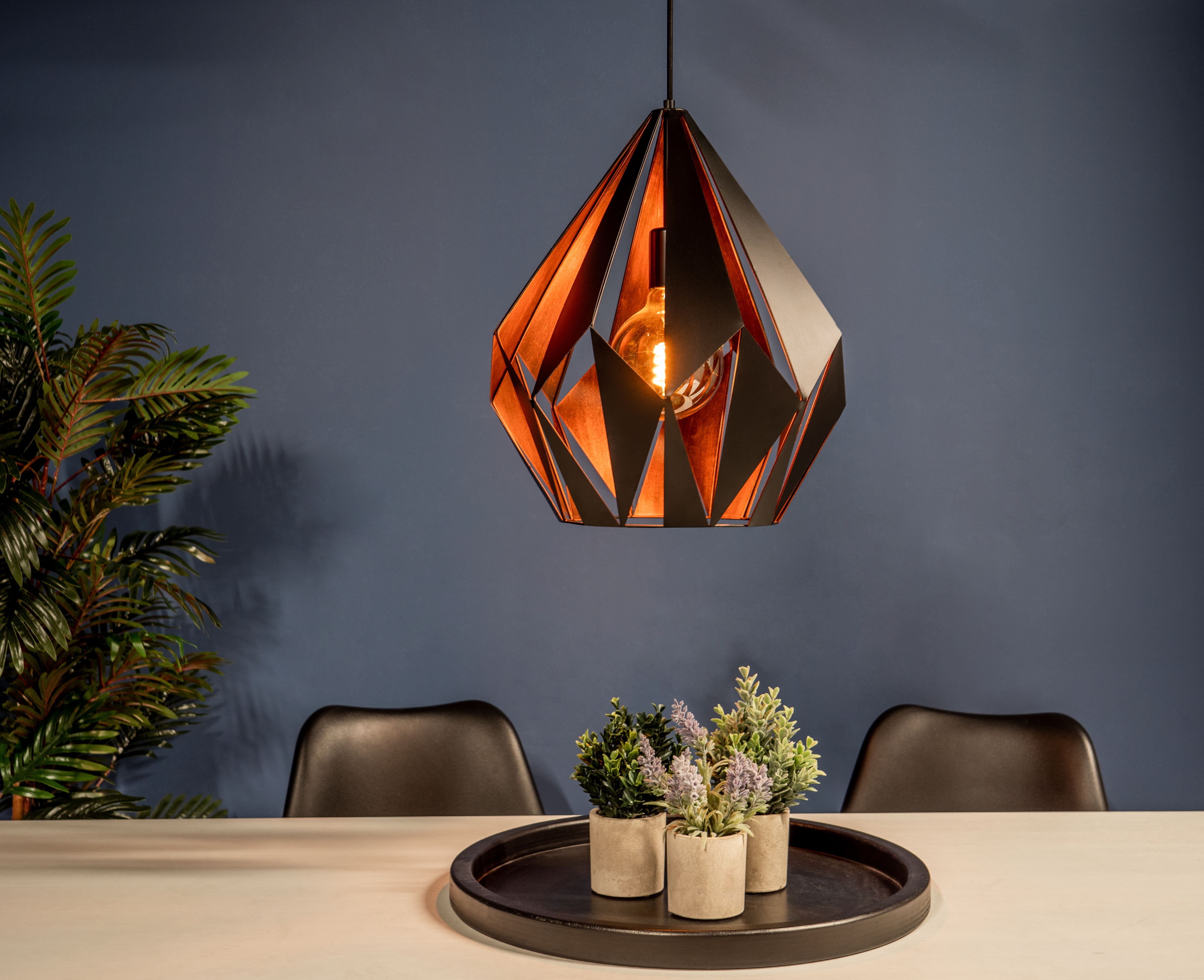 Una sala da pranzo moderna con una lampada geometrica, piante e un vassoio con piccole piante in vaso su un tavolo bianco.