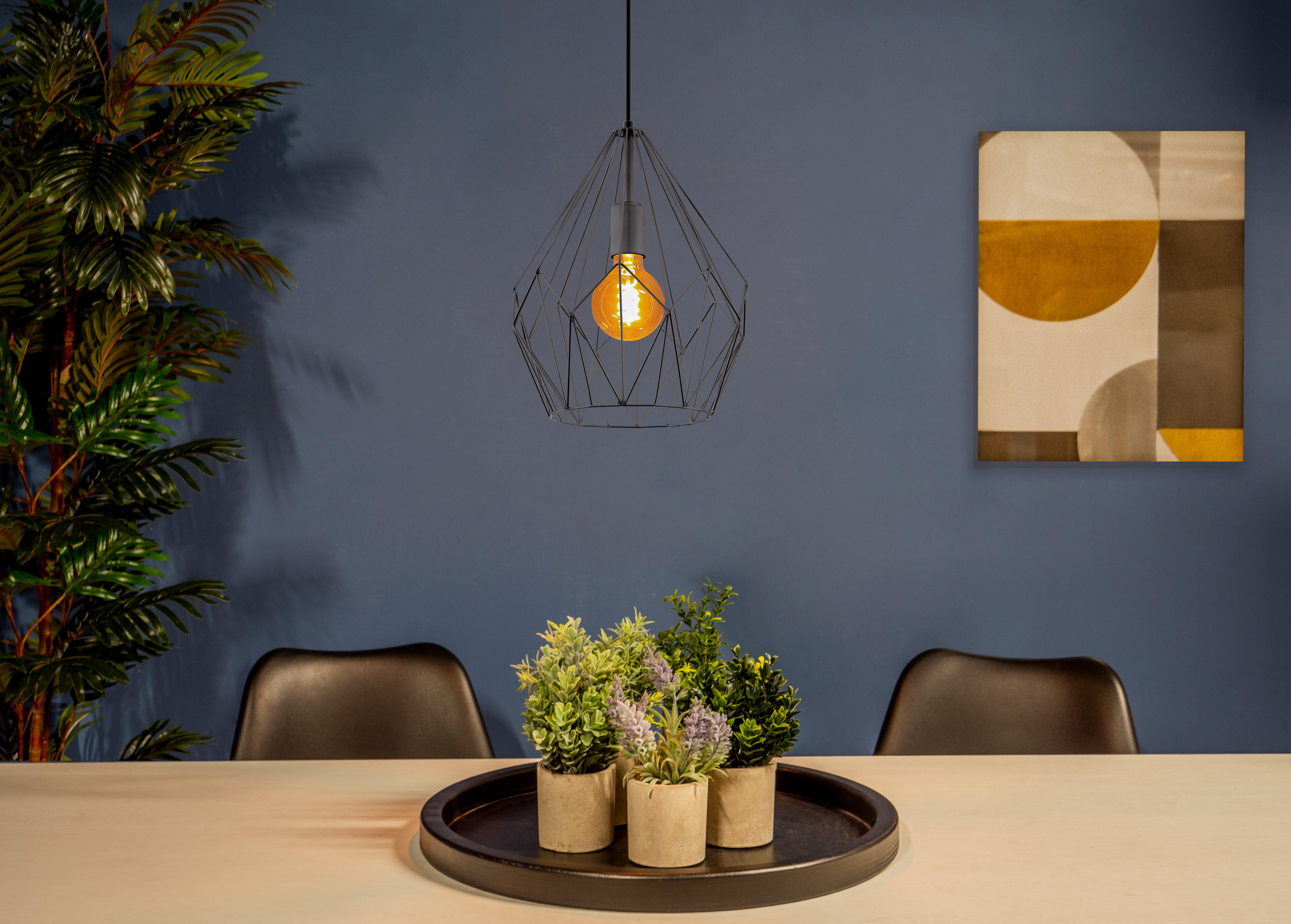 Ein Esszimmer mit Tisch, Pflanzen und geometrischer Leuchte. Blaue Wand mit abstrakter Kunst.