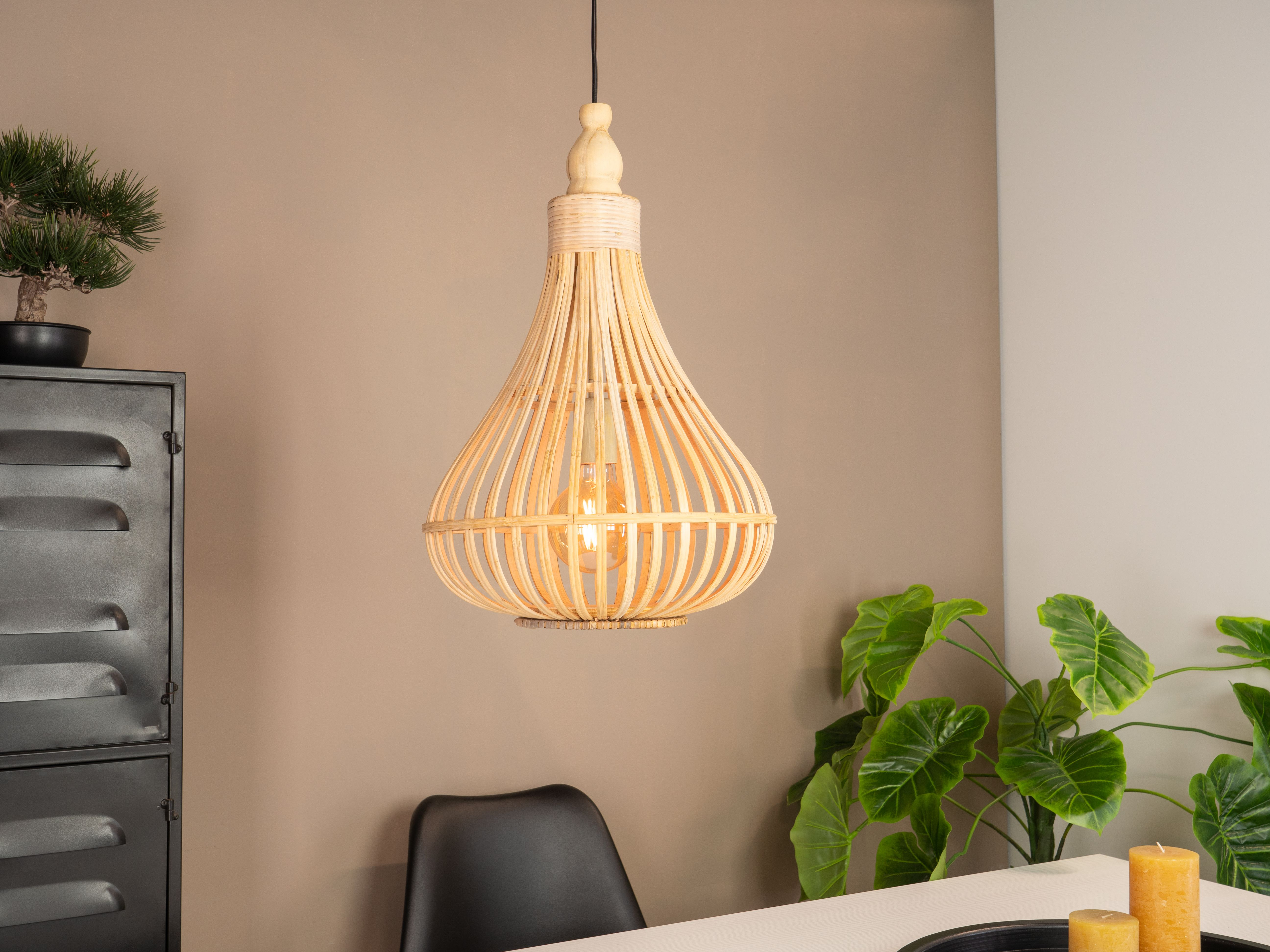 Tkana lampa wisi nad stołem ze świecami i roślinami. Obecna jest również czarna szafka i krzesło.