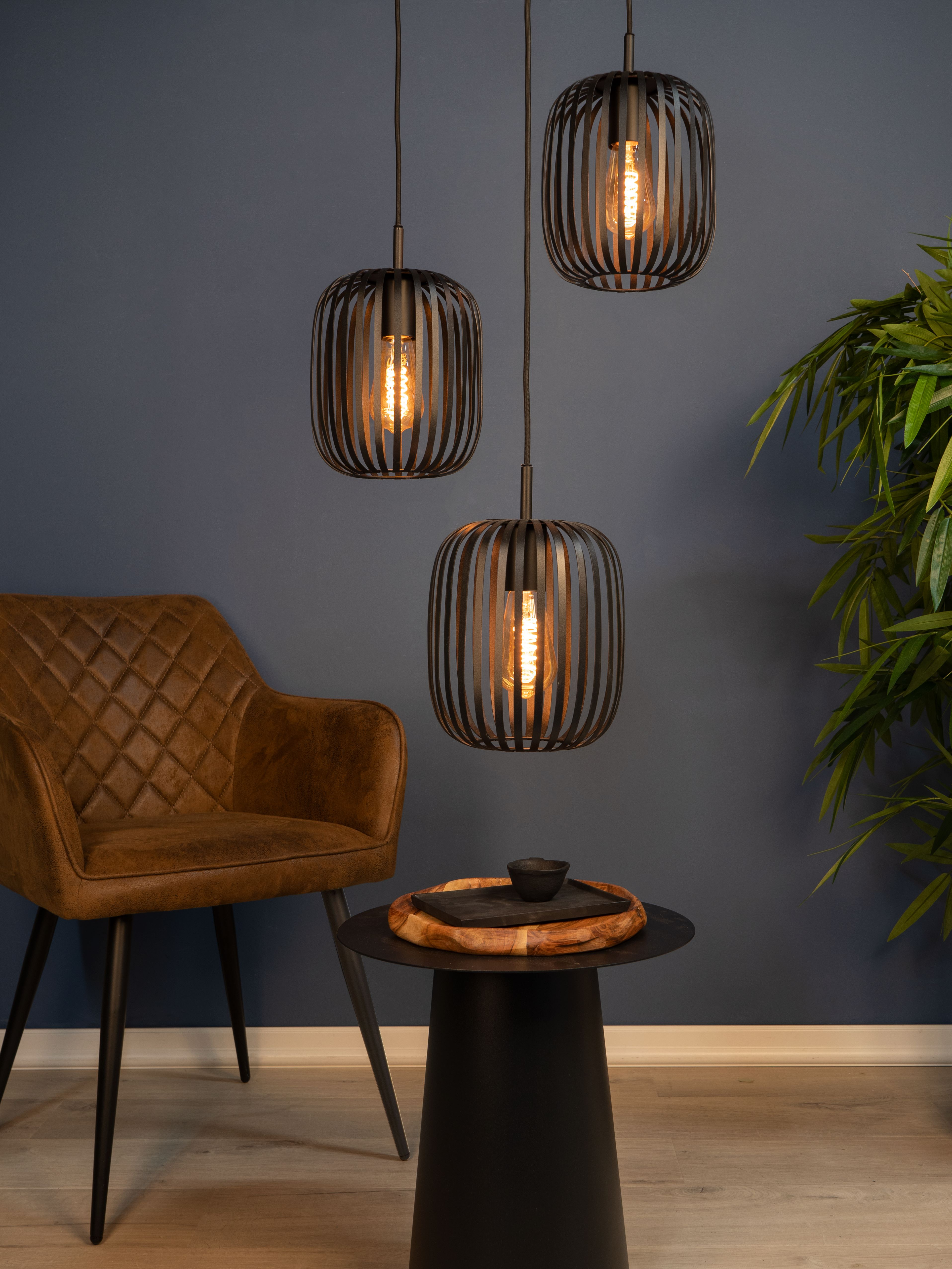 Drie hanglampen met Edison-lampen, bruine stoel, kleine tafel met dienblad en een plant tegen een donkerblauwe muur.