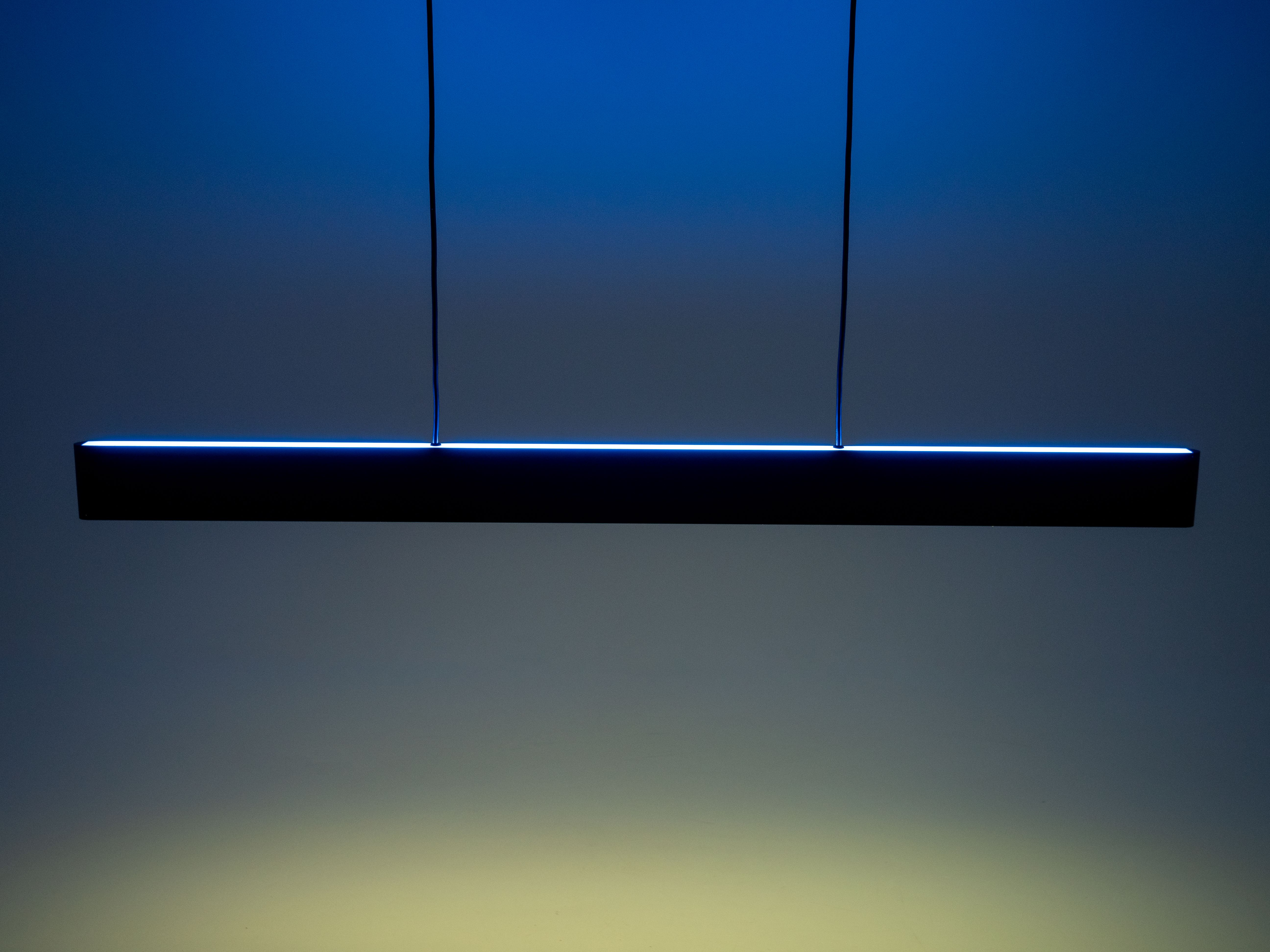 Un luminaire noir moderne est suspendu à deux fils. La lumière émet une lueur bleue. Le fond est dégradé.