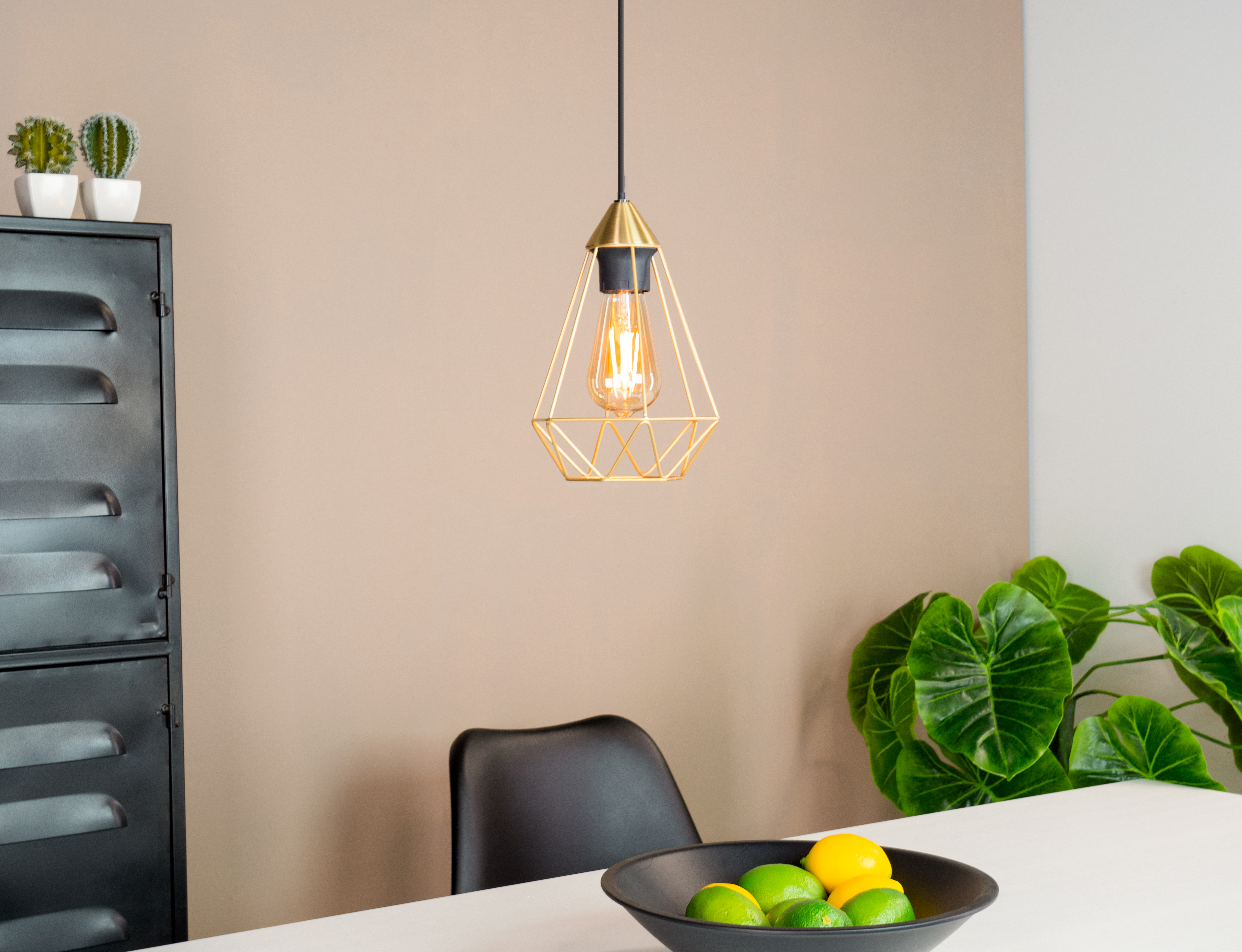 Moderne Küchenszene. Über einem Tisch mit einer Schale mit Zitronen und Limetten hängt eine goldene Pendelleuchte.