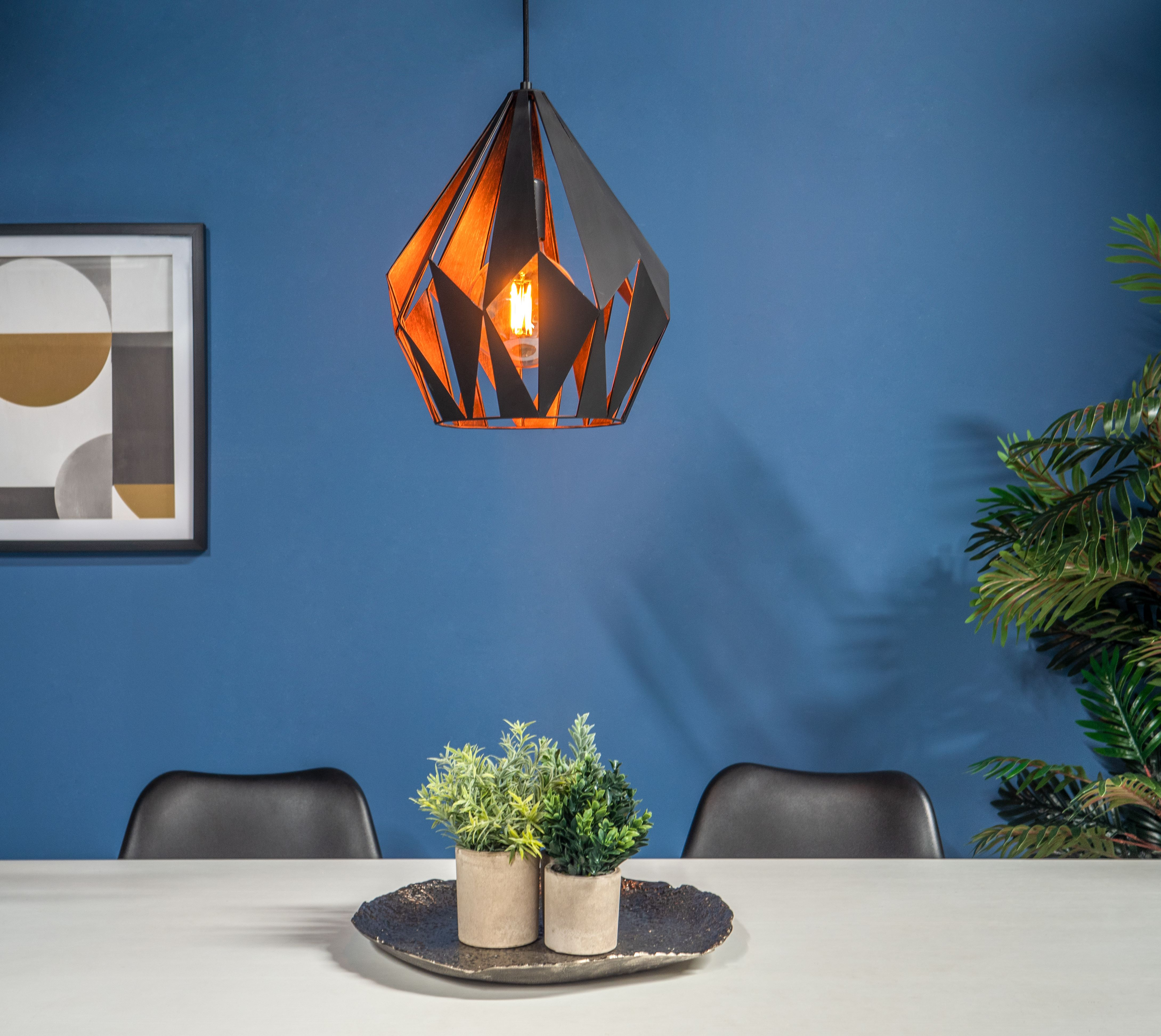 Moderner Esszimmerblick mit geometrischer Pendelleuchte, Pflanzen und einem gerahmten abstrakten Kunstwerk.