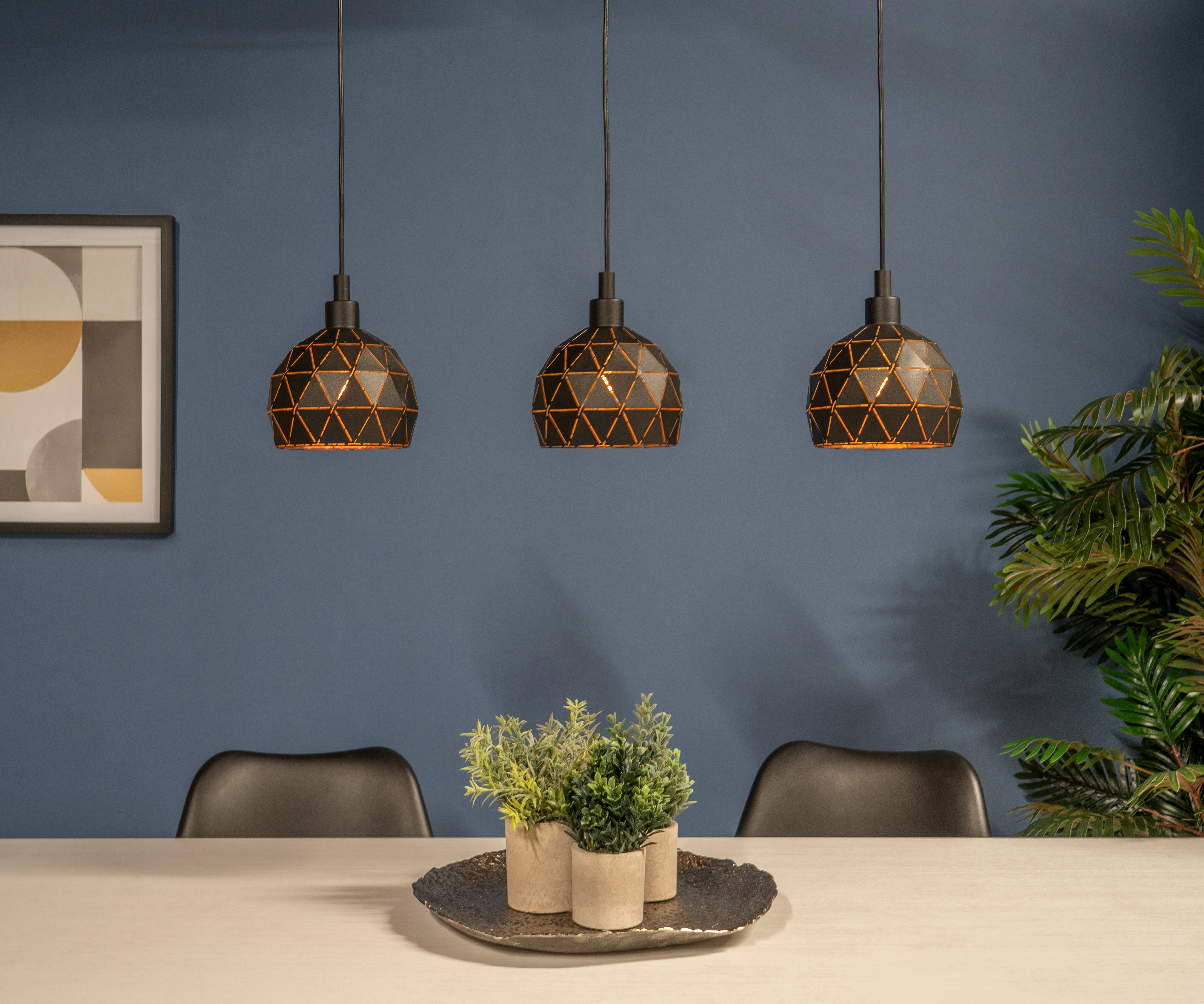 Drei Hängelampen hängen über einem Tisch mit Pflanzen. Ein Gemälde und eine Pflanze sind an der blauen Wand.