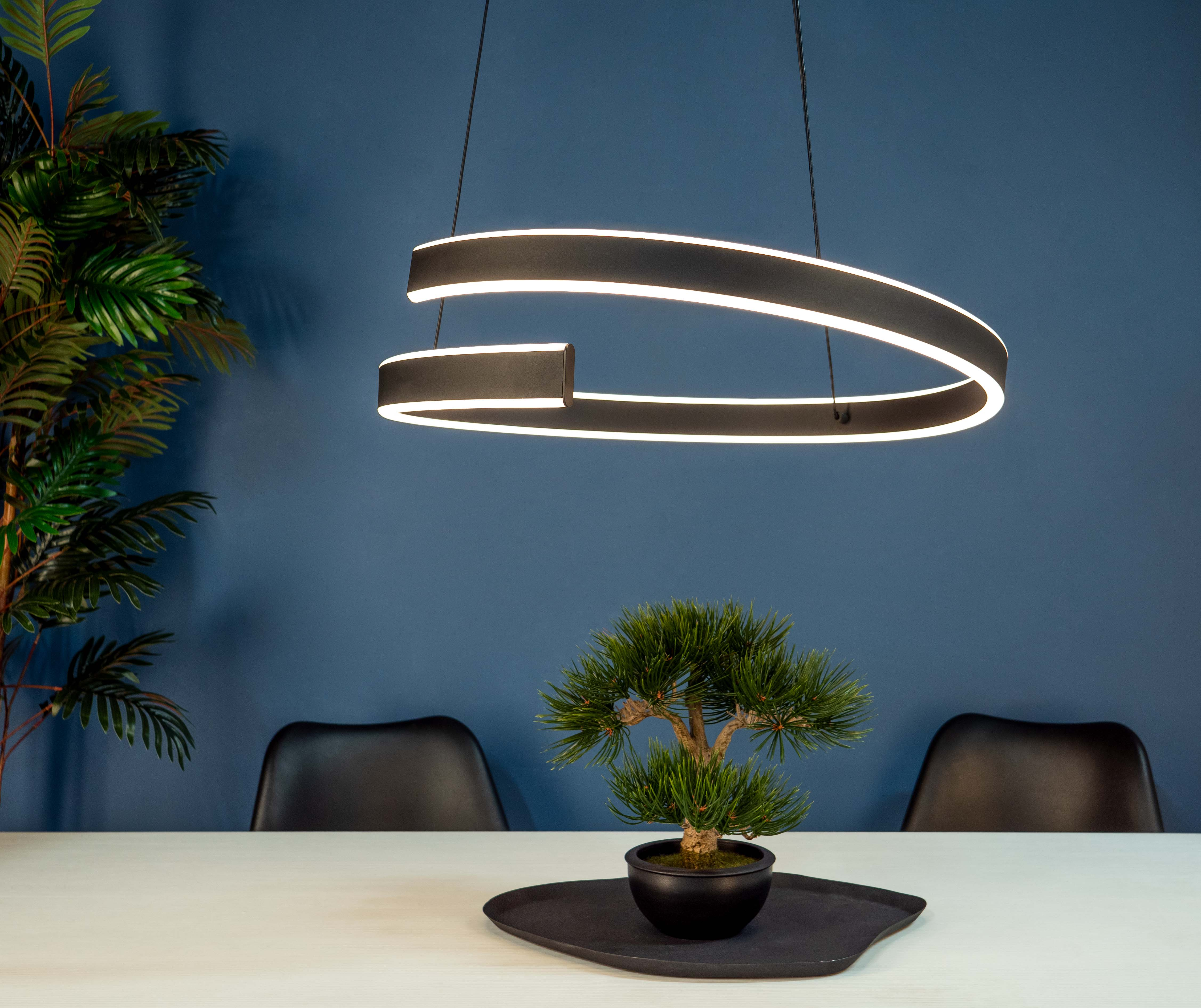 Ein modernes Zimmer mit einem Bonsai auf einem Tisch. Eine schwarze Leuchte hängt von der Decke.