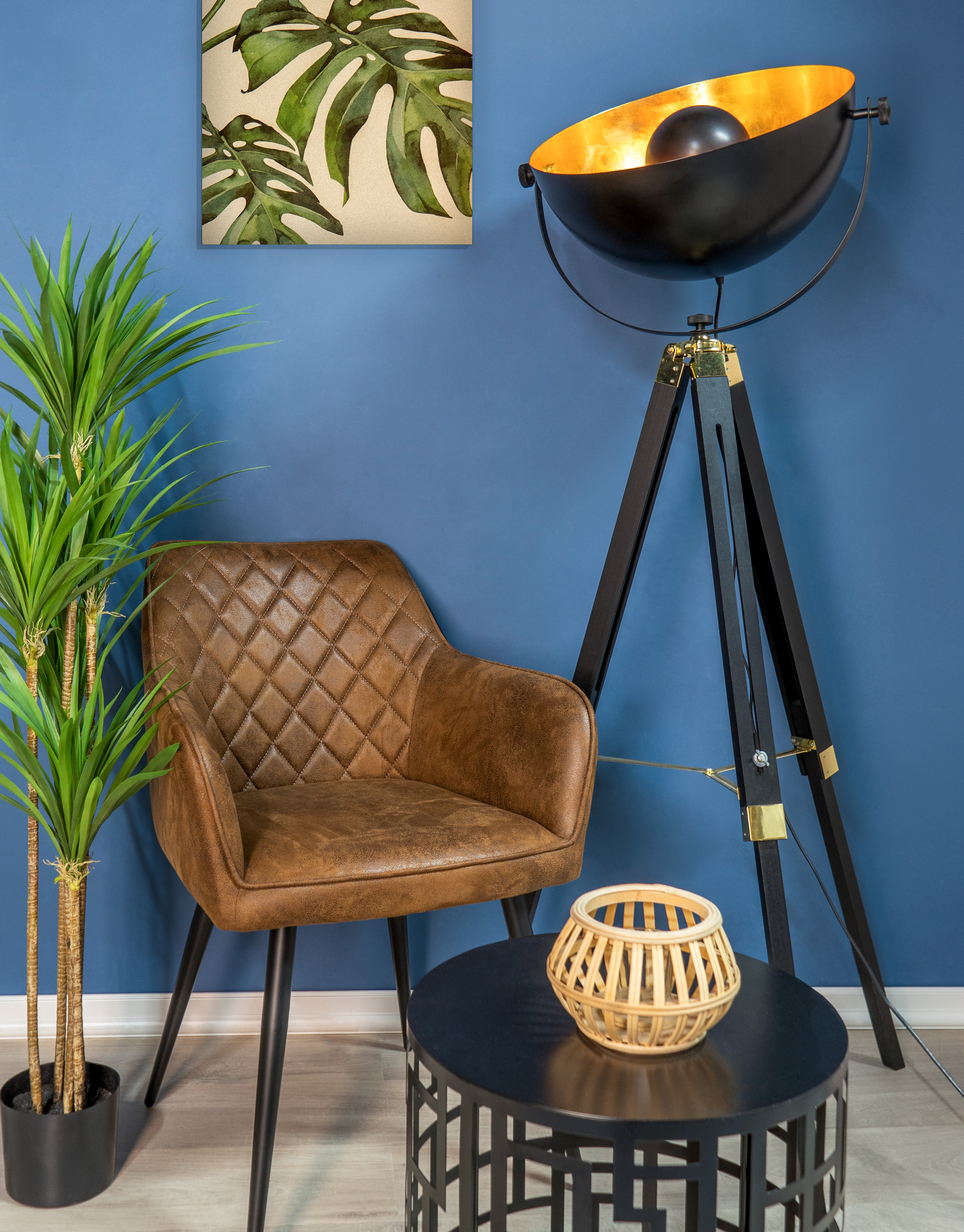 Una habitación con una silla, lámpara y mesa. Hay una planta y un cuadro en la pared.