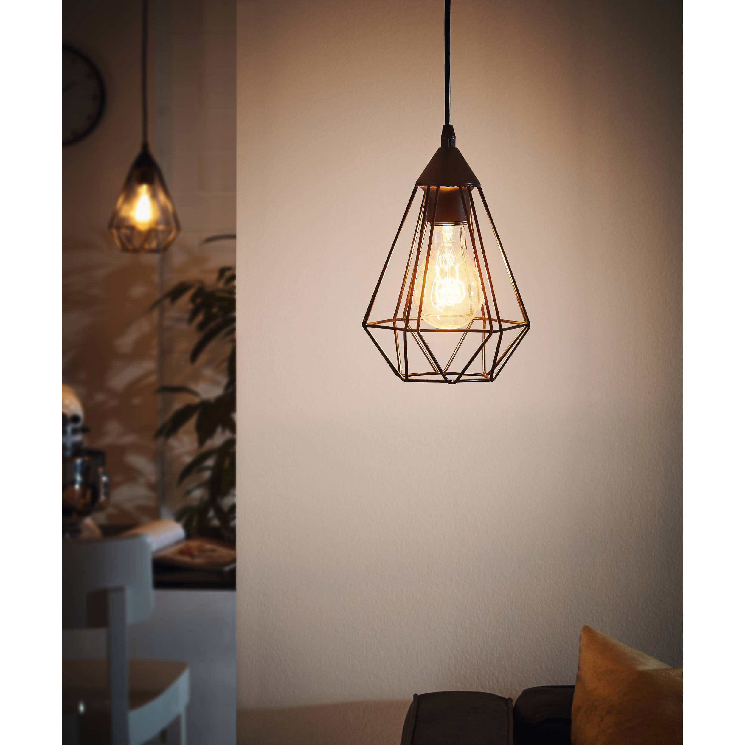 Una lampada a sospensione con un paralume a gabbia è appesa in una stanza. La luce è accesa.