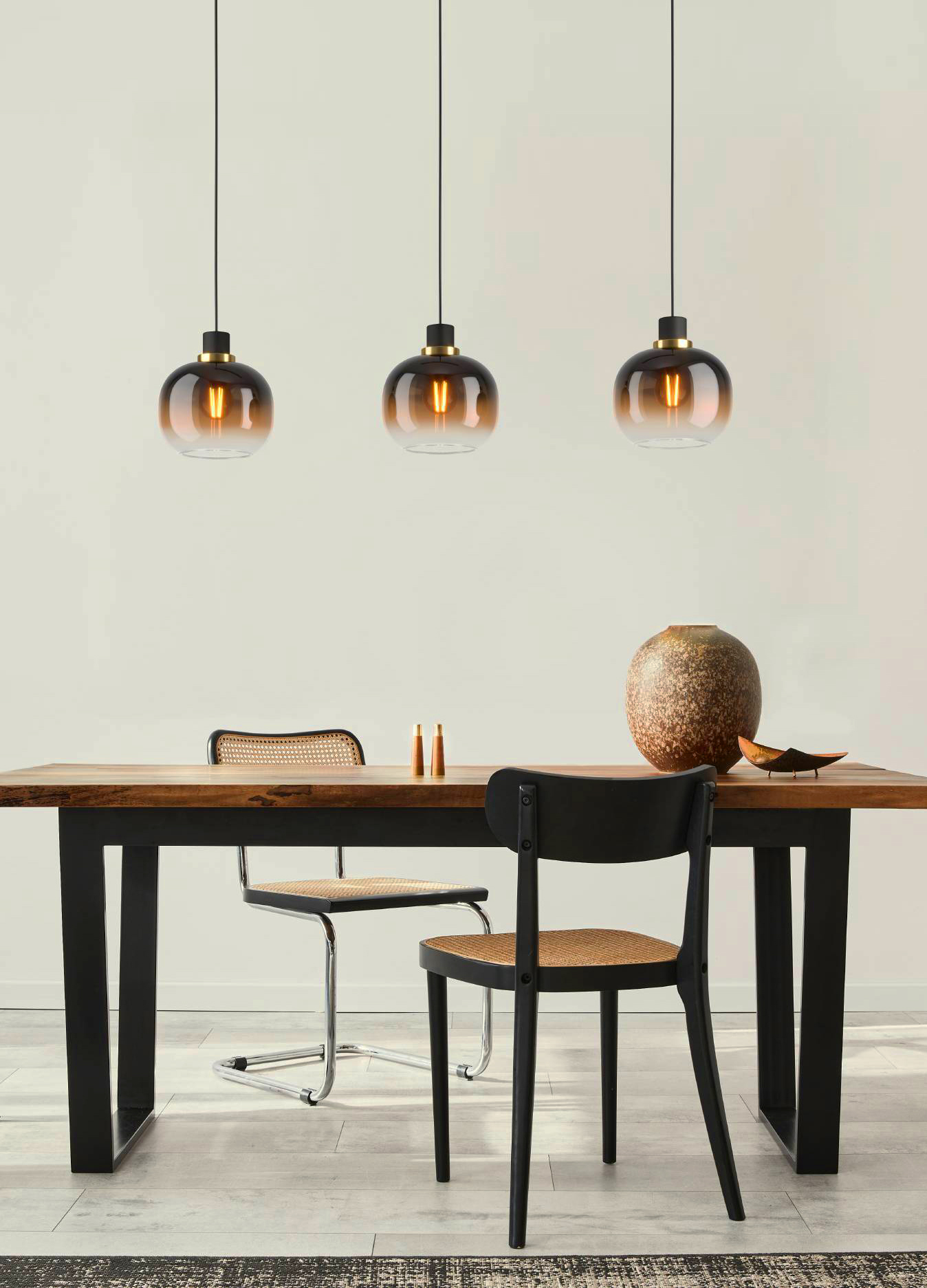 Esszimmer-Szene mit Holztisch, Stühlen und drei Pendelleuchten. Eine Vase und Dekoration auf dem Tisch.