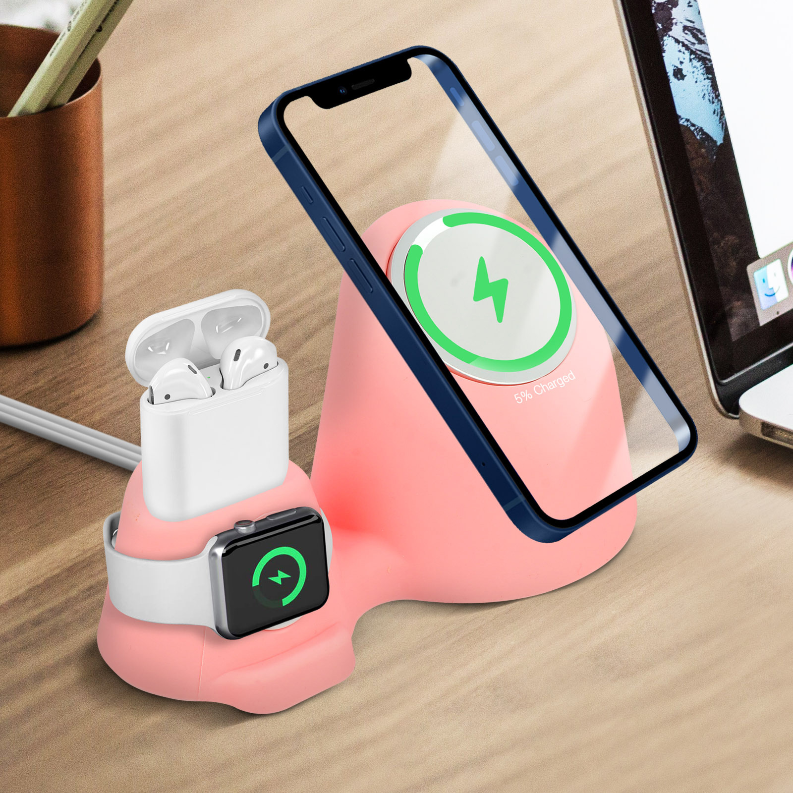 Estación de carga rosa con teléfono, reloj y auriculares. El teléfono muestra la carga, el reloj se está cargando. Fondo de escritorio de madera.