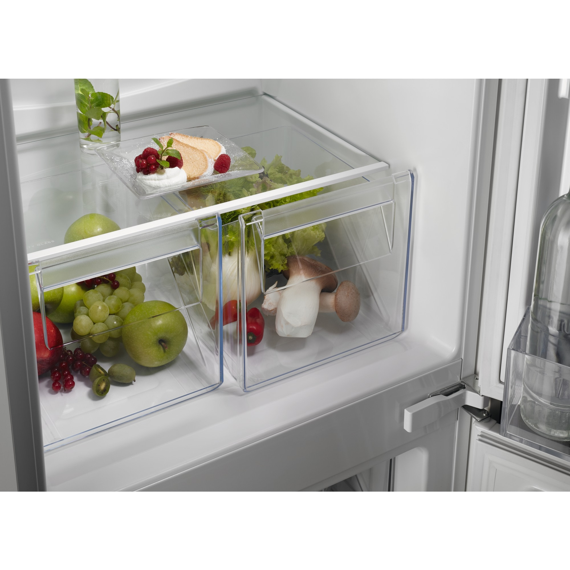Interior de refrigerador con frutas, verduras y pastel. Manzanas verdes, uvas y lechuga son visibles en cajones.