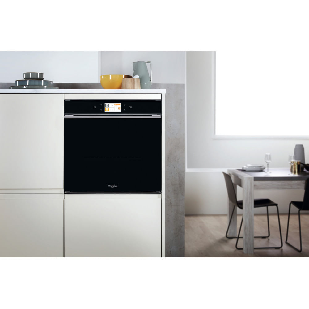 Une cuisine moderne présente un four noir, une table à manger et divers ustensiles de cuisine sur un comptoir blanc.