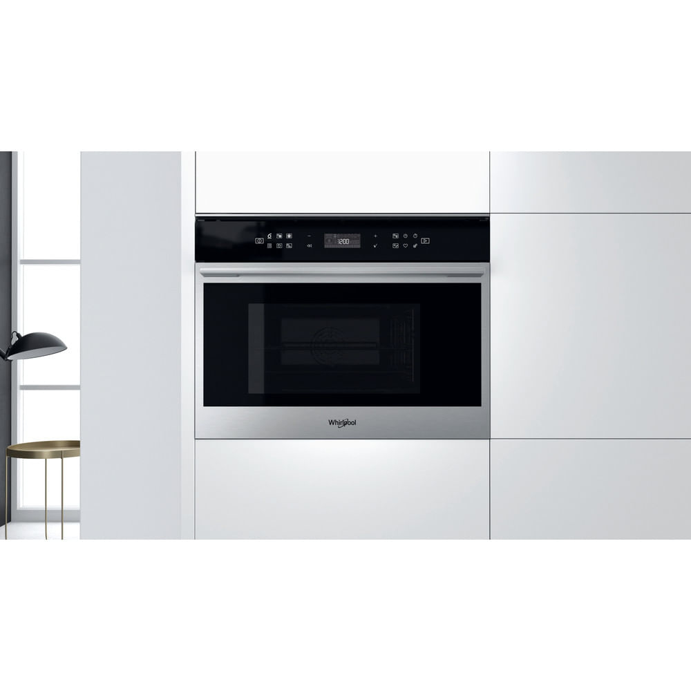 Un four à micro-ondes Whirlpool encastré dans des armoires de cuisine blanches. Le four a une porte en verre noir et un affichage numérique.