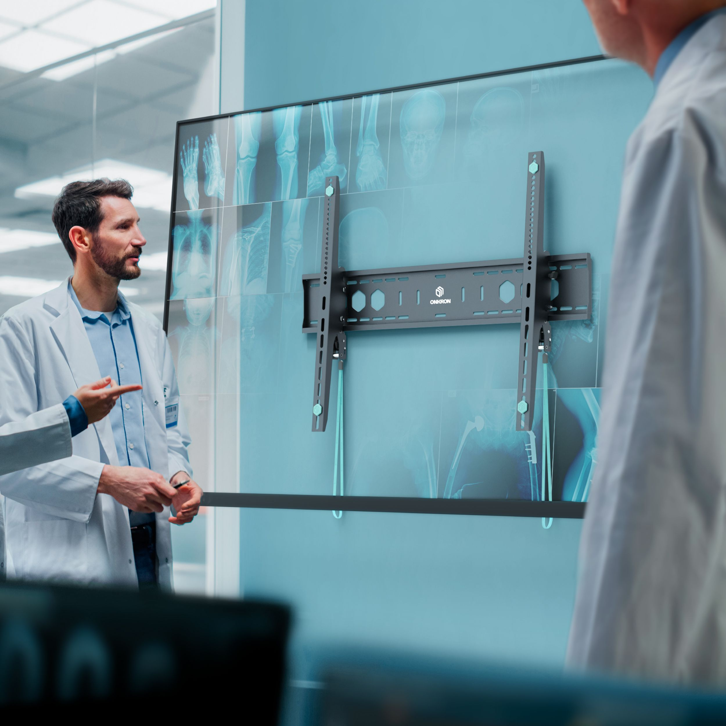 Lekarze w białych kitlach badają zdjęcia rentgenowskie na ekranie z uchwytem ściennym. Jeden wskazuje i tłumaczy.
