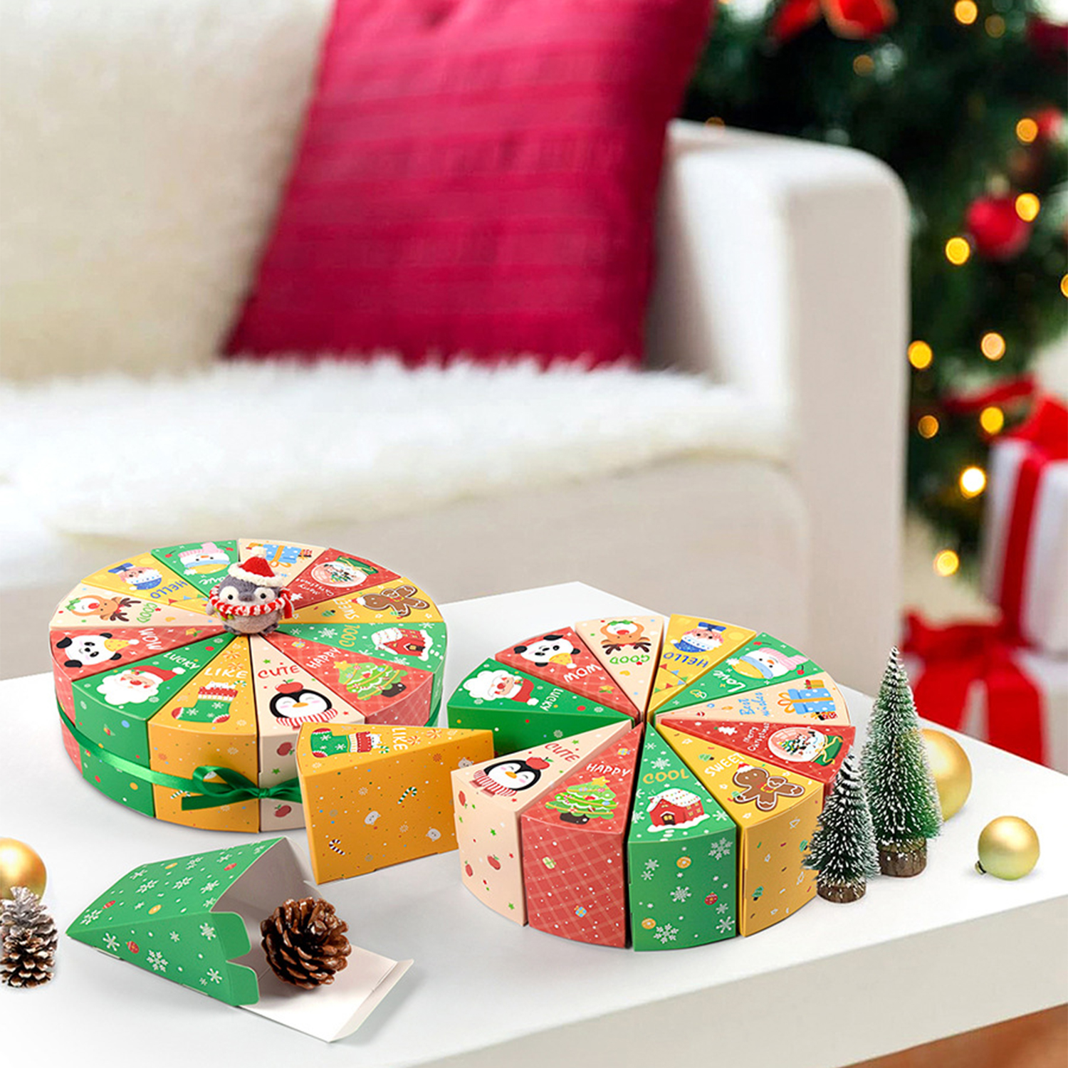 Festliche Schachteln in Form von Kuchenstücken. Ein Pinguin oben drauf. Weihnachtsbaum, Geschenke und Ornamente im Hintergrund. Ein rotes Kissen auf einem weißen Sofa.