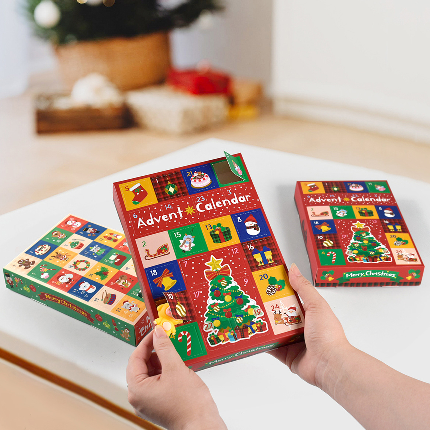 Hände halten einen roten Adventskalender mit Weihnachtsbaum-Illustration, umgeben von zwei ähnlichen Boxen. Frohe Weihnachten Text ist sichtbar.