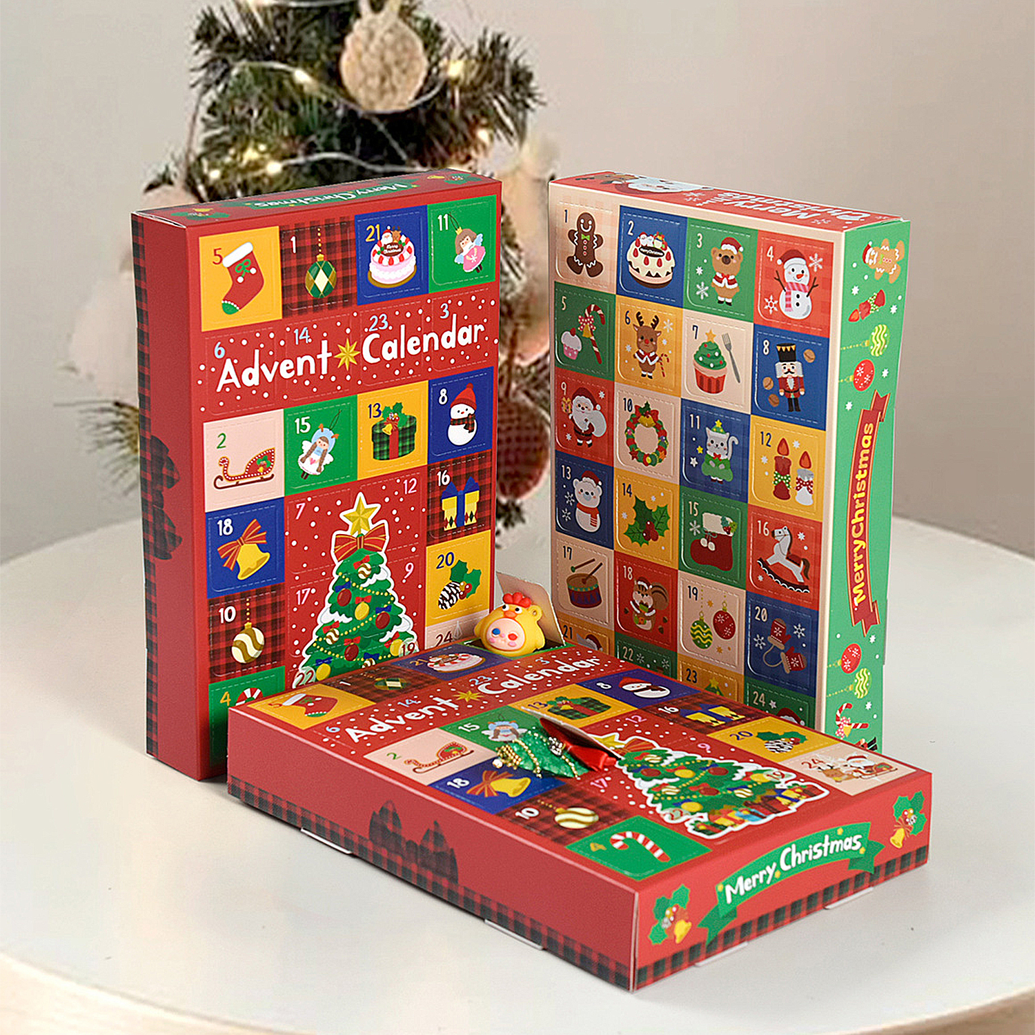 Drei Weihnachtskalender auf einem weißen Tisch. Die Kalender sind rot mit bunten Quadraten und festlichen Bildern.