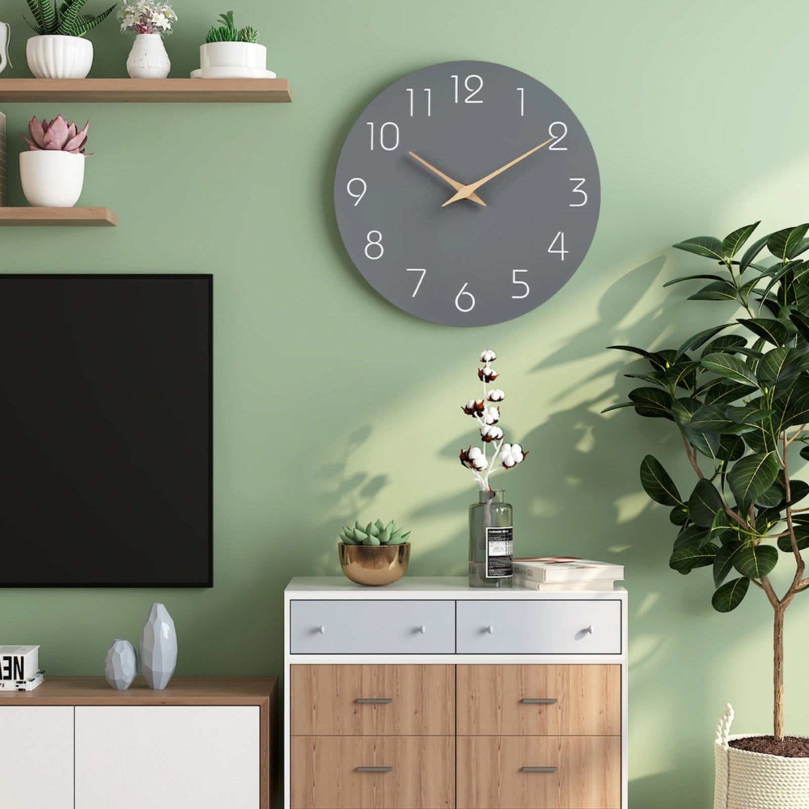 Graue Uhr an grüner Wand. Darunter ein weißer Schrank mit Deko und einer Pflanze. Rechts eine große Pflanze.
