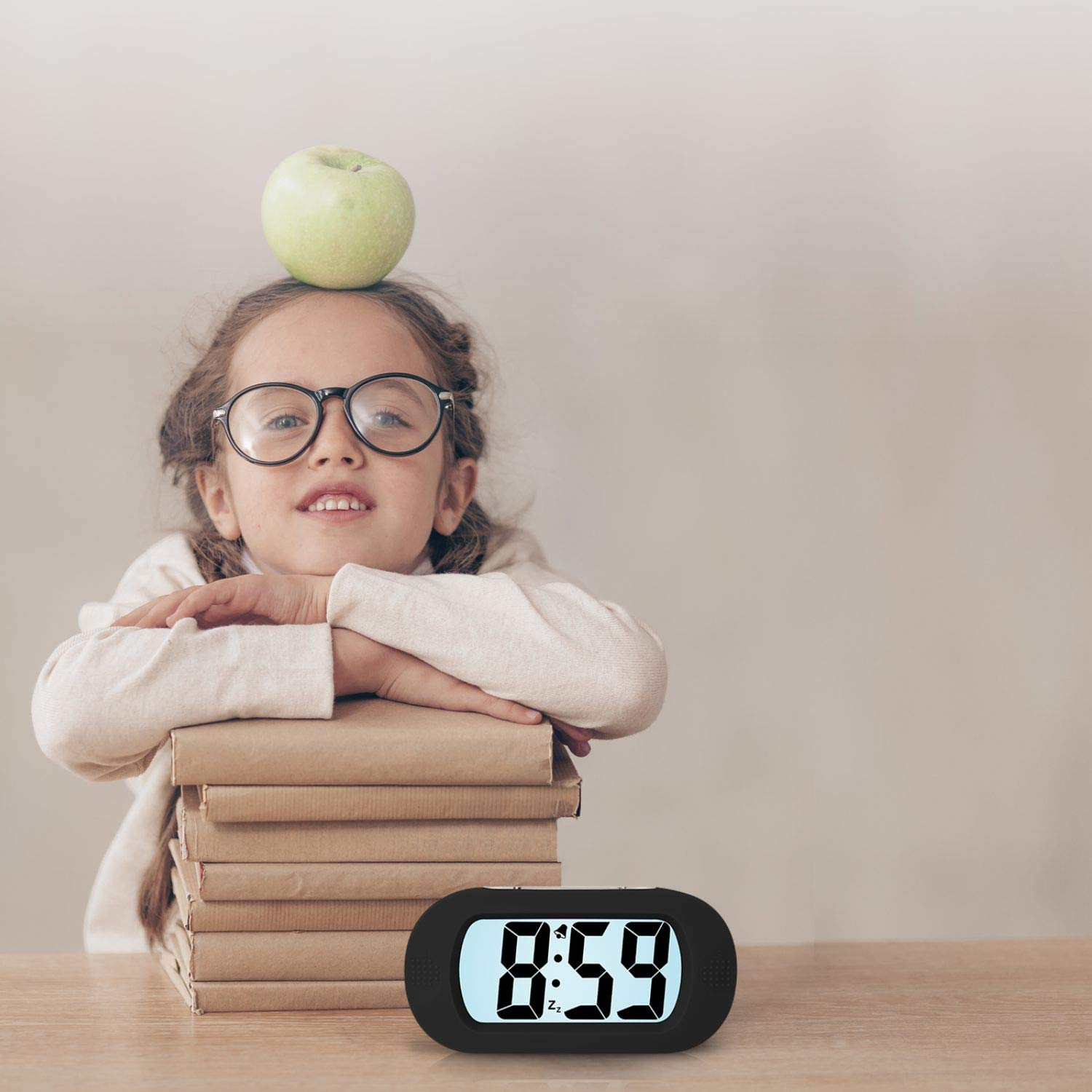 Una ragazza con gli occhiali e una mela in testa si appoggia a dei libri. Un orologio digitale segna le 8:59 su un tavolo di legno.