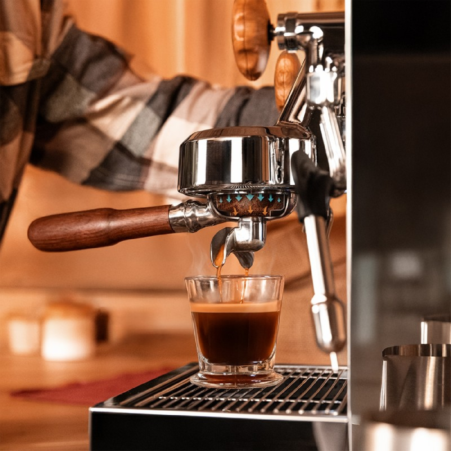 Espressomaschine gibt Kaffee in ein Glas ab. Eine Person bereitet Kaffee zu. Die Szene ist warm getönt und fokussiert.