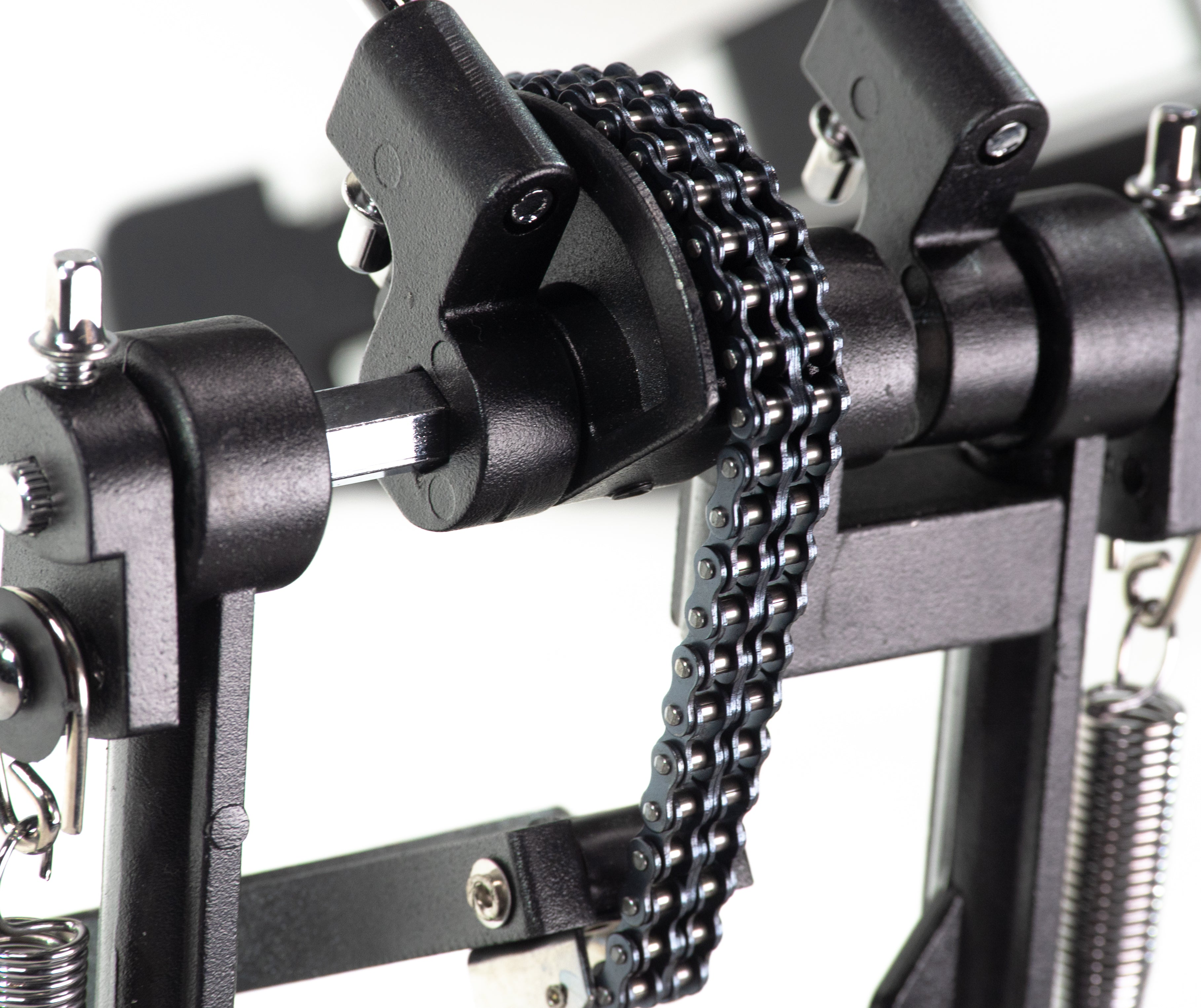 Nahaufnahme eines schwarzen Schlagzeugpedals. Eine Metallkette verbindet zwei Teile. Der Hintergrund ist weiß.