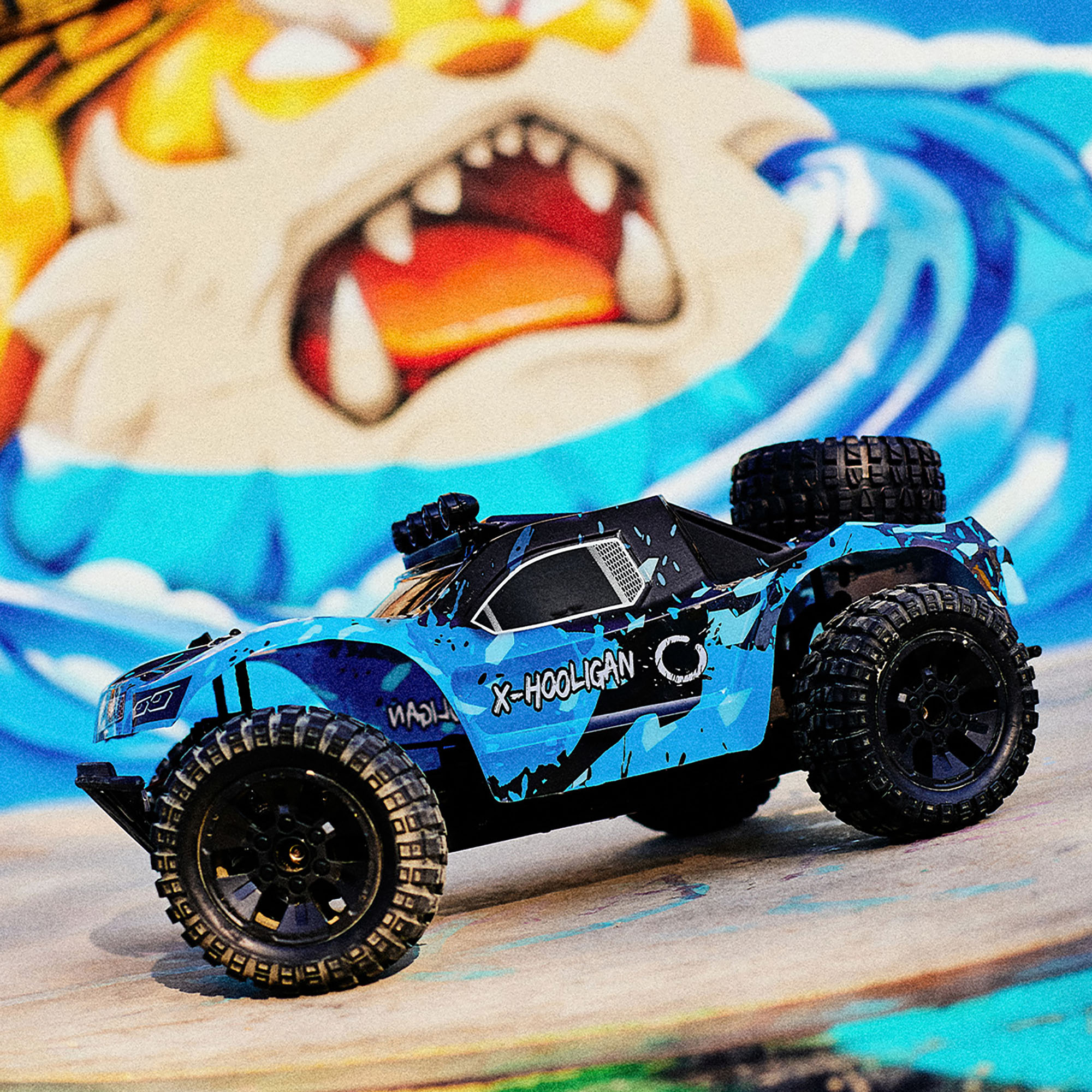 Ein blau-schwarzes X-Hooligan RC-Auto auf einer Oberfläche mit Graffiti-Hintergrund eines Monstergesichts.