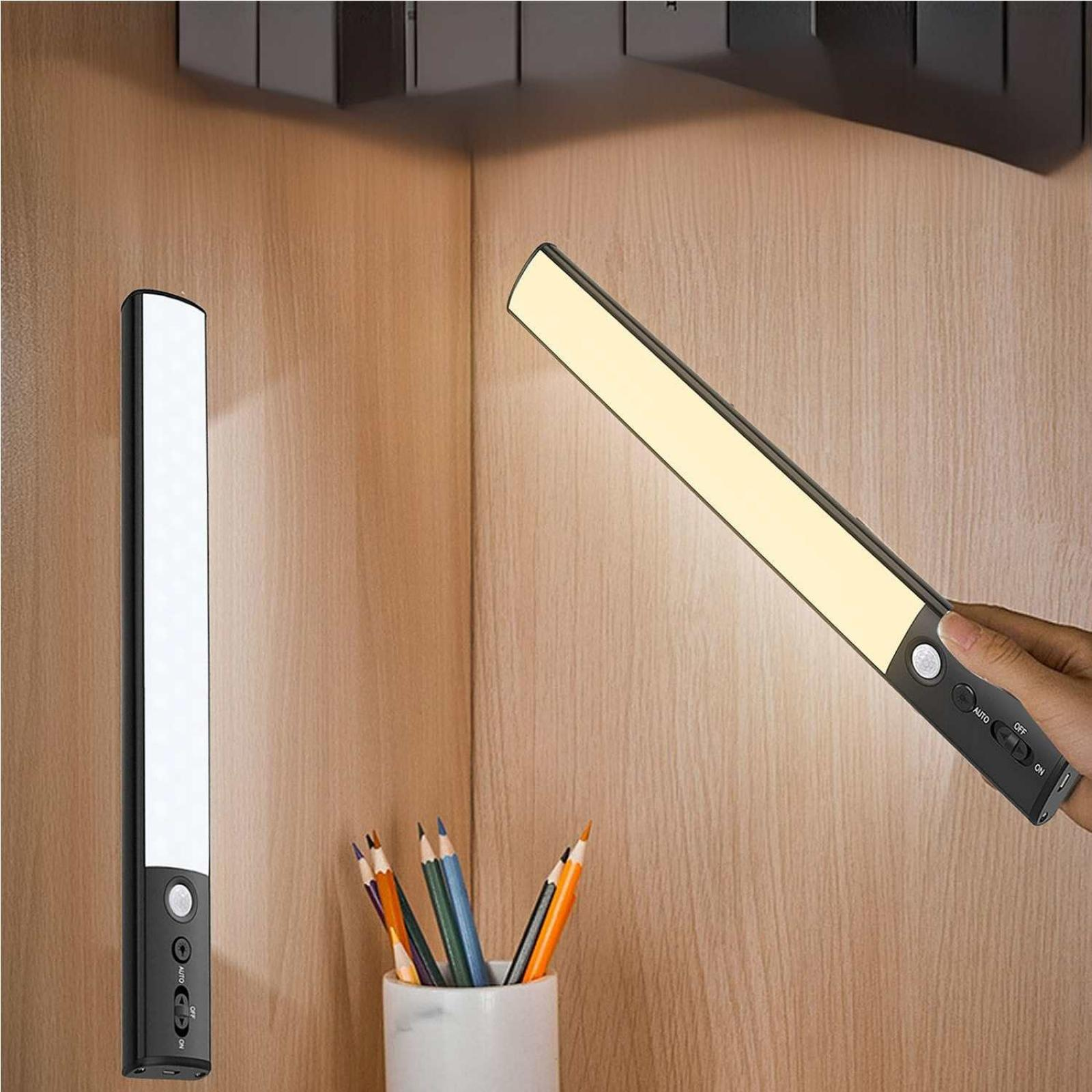 Zwei LED-Leuchten auf Holz. Eine Leuchte wird von einer Hand gehalten. Bleistifte in einem weißen Becher.