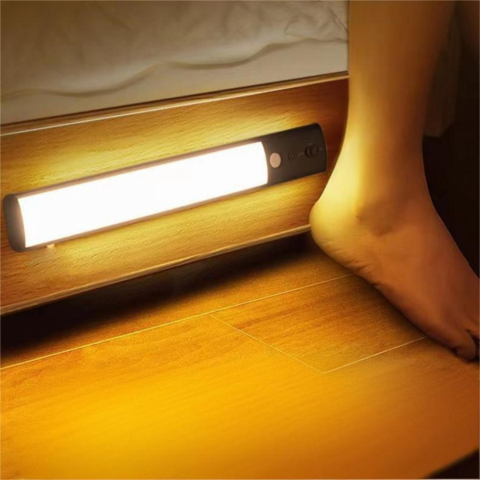 Ein beleuchteter LED-Streifen ist unter einem Bettrahmen montiert. Ein Fuß befindet sich in der Nähe des Rahmens auf einem Holzboden.