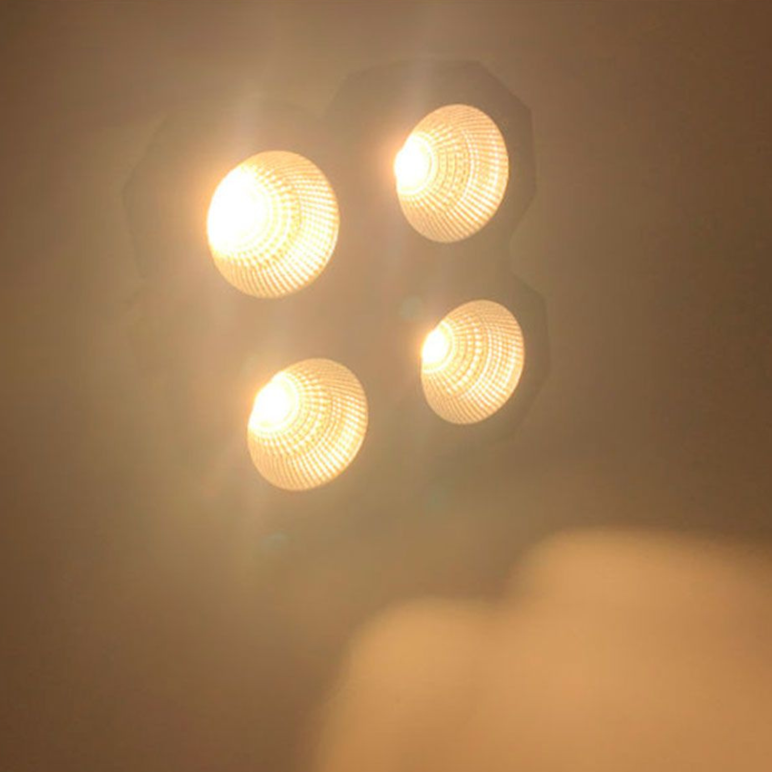 Vier helle, kreisförmige Lichter, die warmes Licht aussenden, vor einem gedämpften Hintergrund.