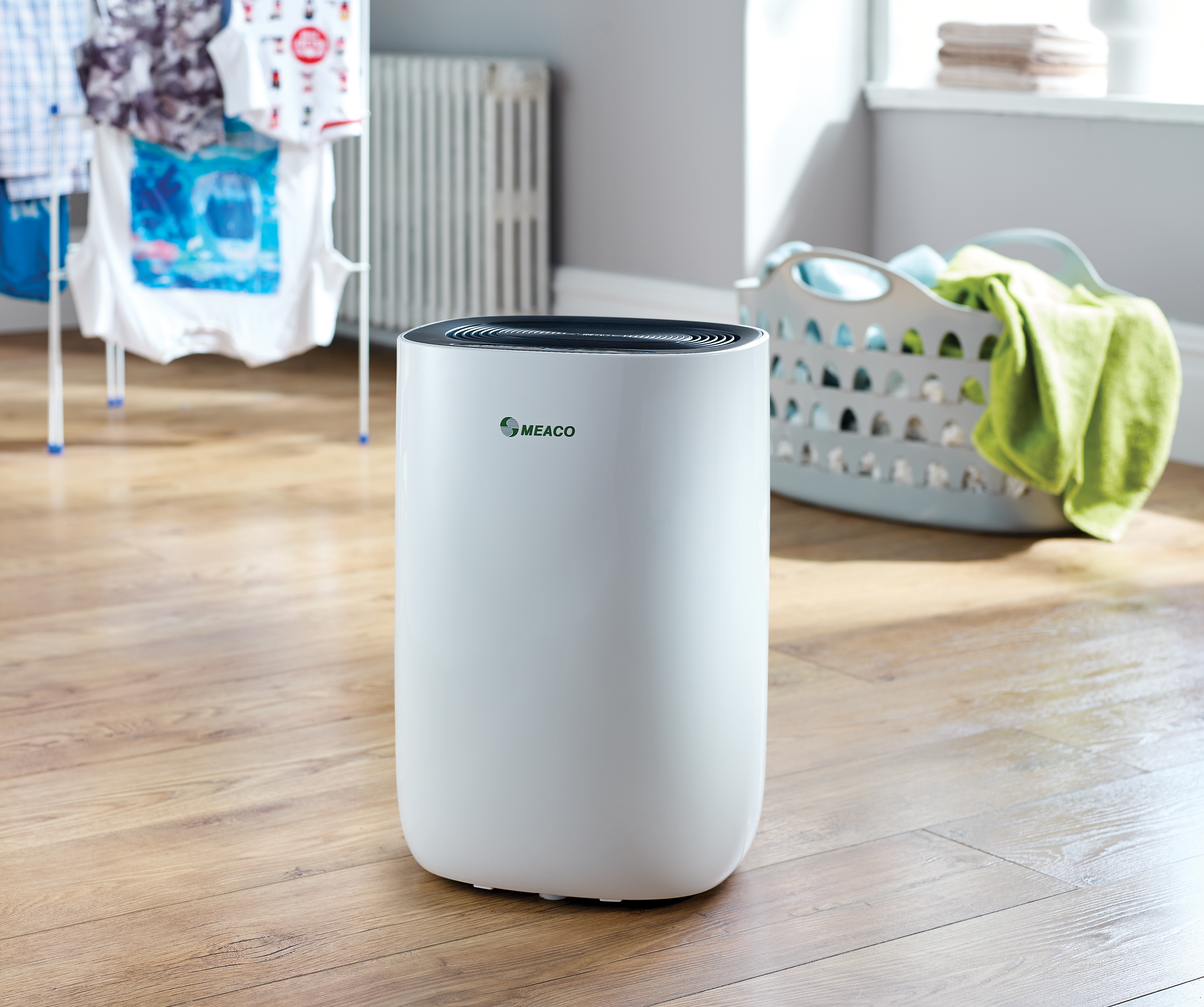 Biały oczyszczacz powietrza w pokoju z suszącym się praniem i koszem na pranie z zielonym ręcznikiem.