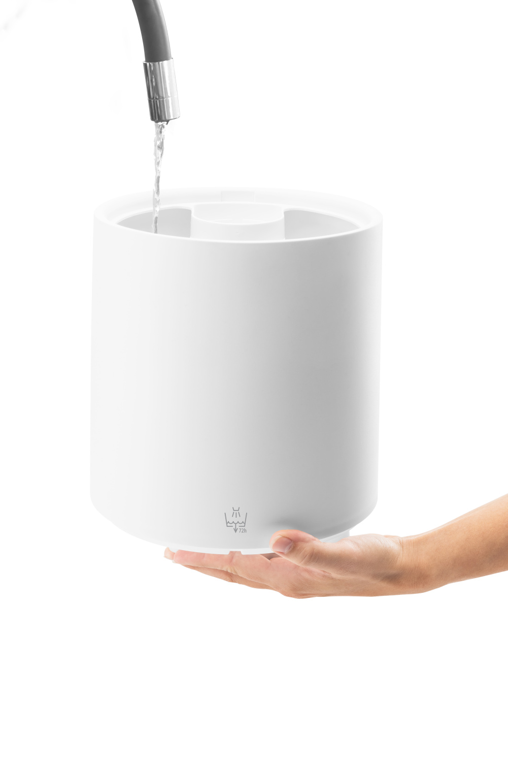 Un umidificatore bianco è tenuto in una mano. L'acqua vi scorre da un rubinetto. Lo sfondo è bianco.
