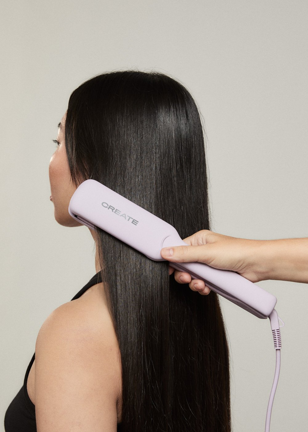 Una persona se alisa el pelo negro con una plancha de pelo morada. La plancha tiene la palabra 'CREATE'.
