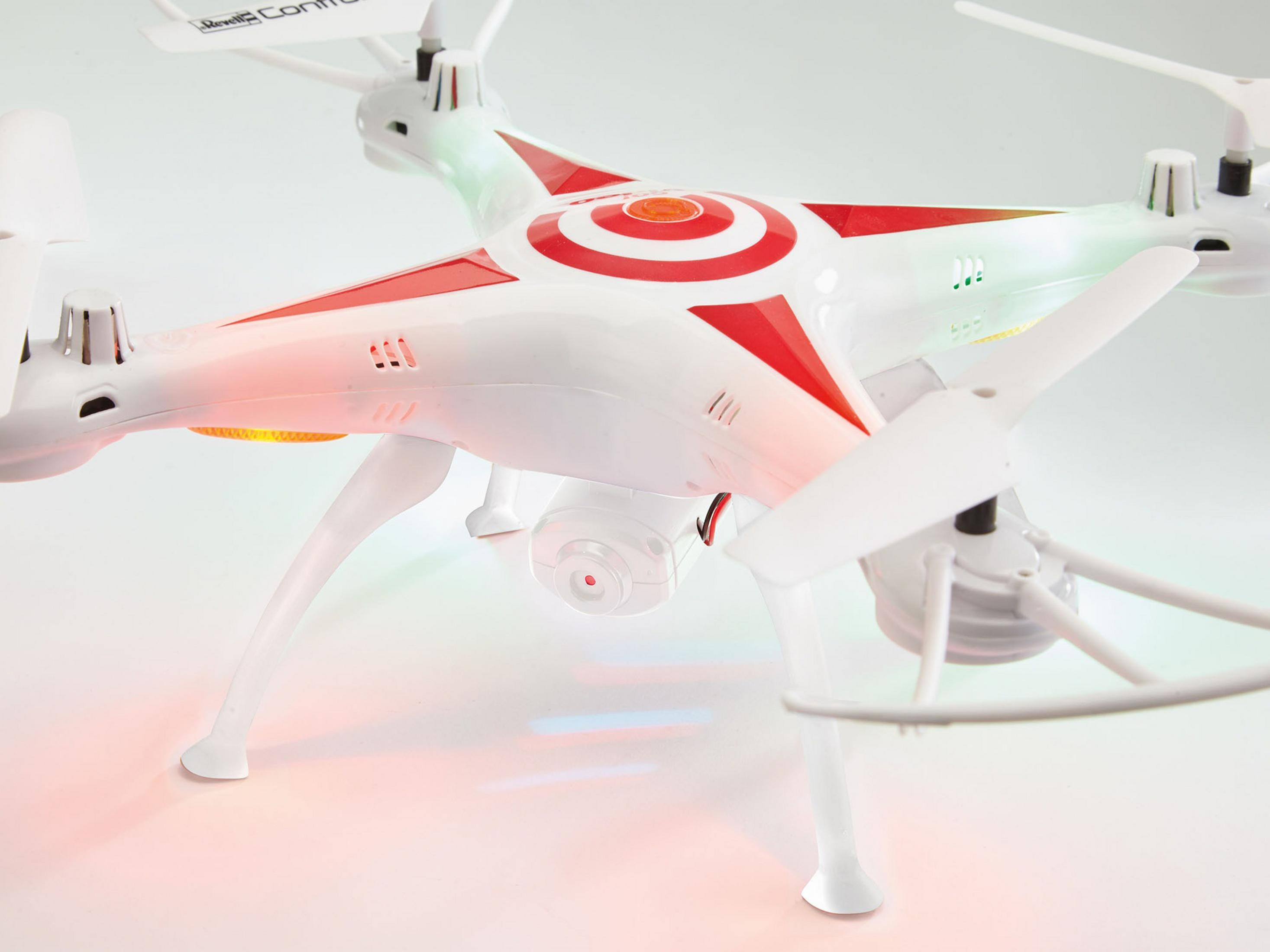 Biały dron z czerwonymi akcentami i tarczą na górze, śmigłami i kamerą. Tło jest białe.